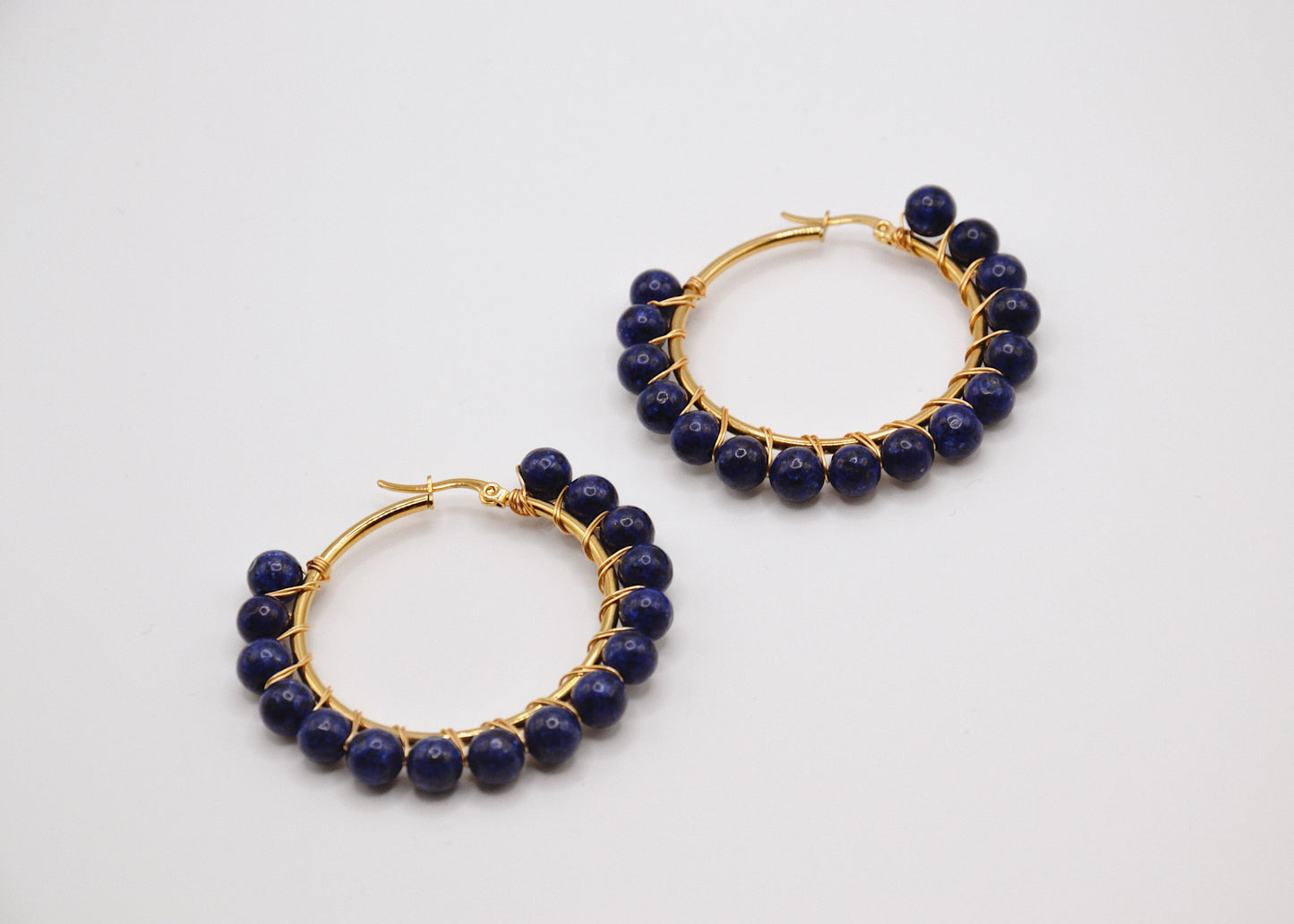 Boucles d’oreilles créoles dorées avec perles rondes bleu marine sur fond blanc