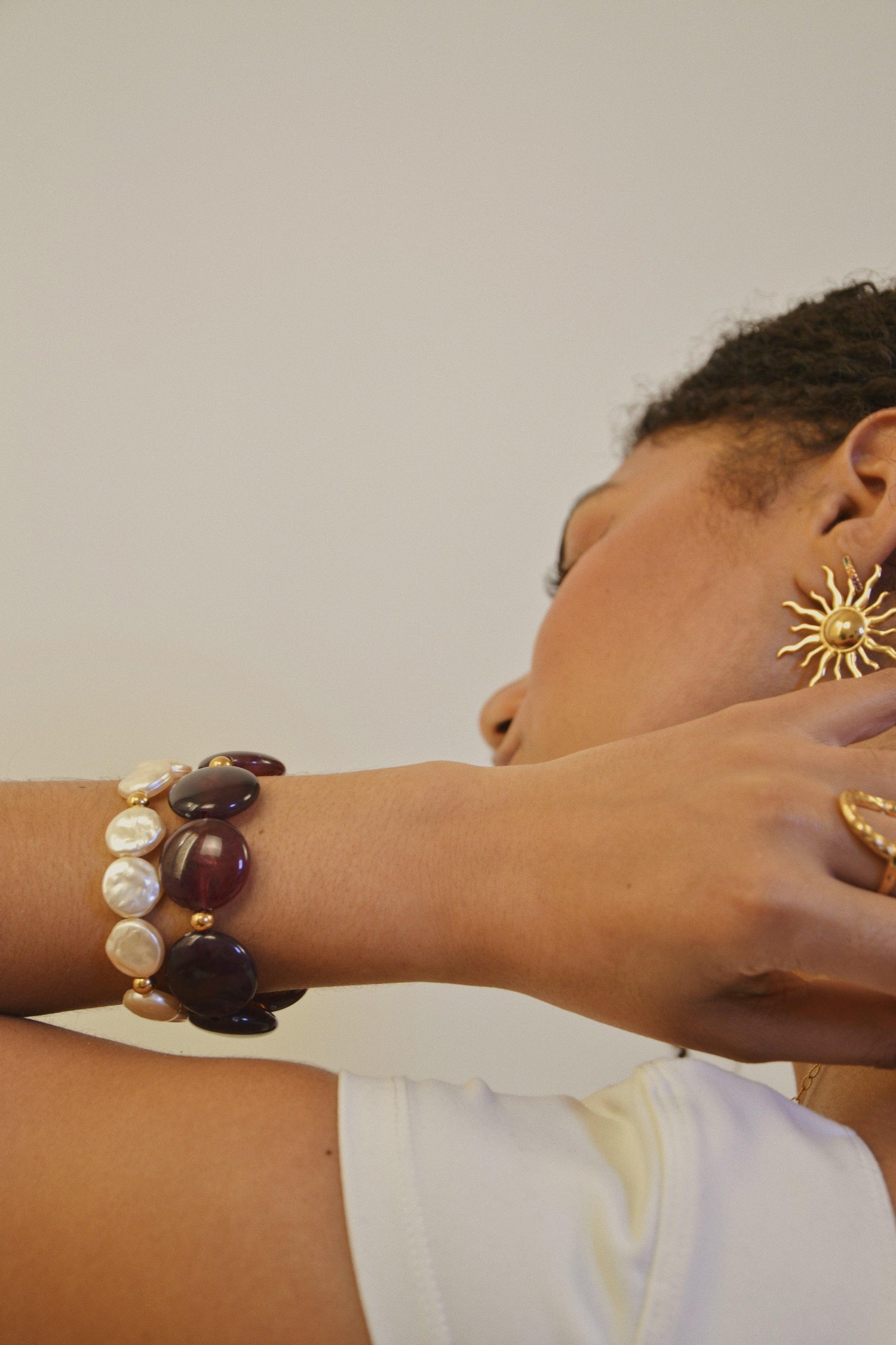 Femme portant boucles d’oreilles soleil dorées, bracelets perles et pierres, bague dorée