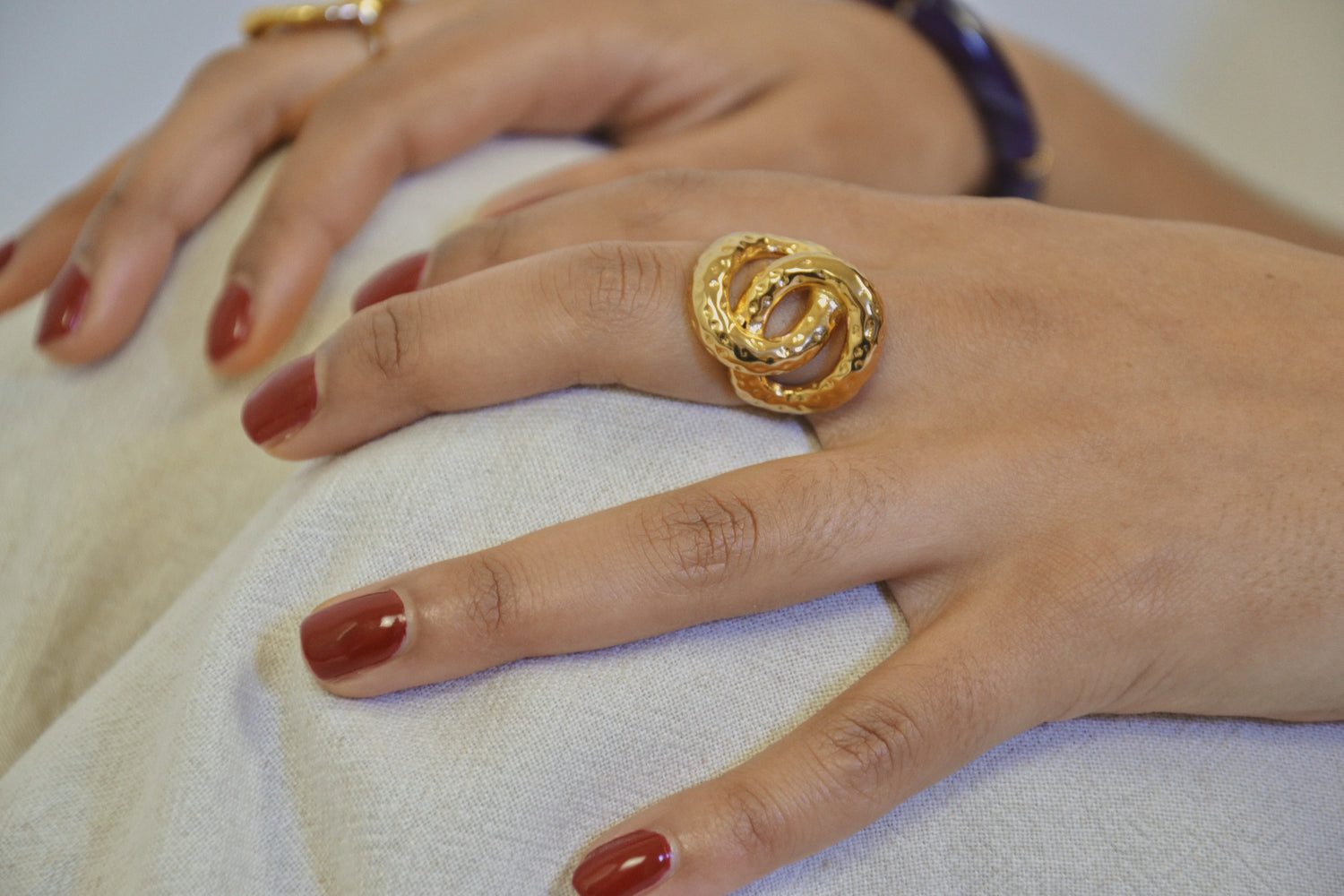 Main posant une bague dorée surdimensionnée, ongles vernis rouge, fond clair élégant