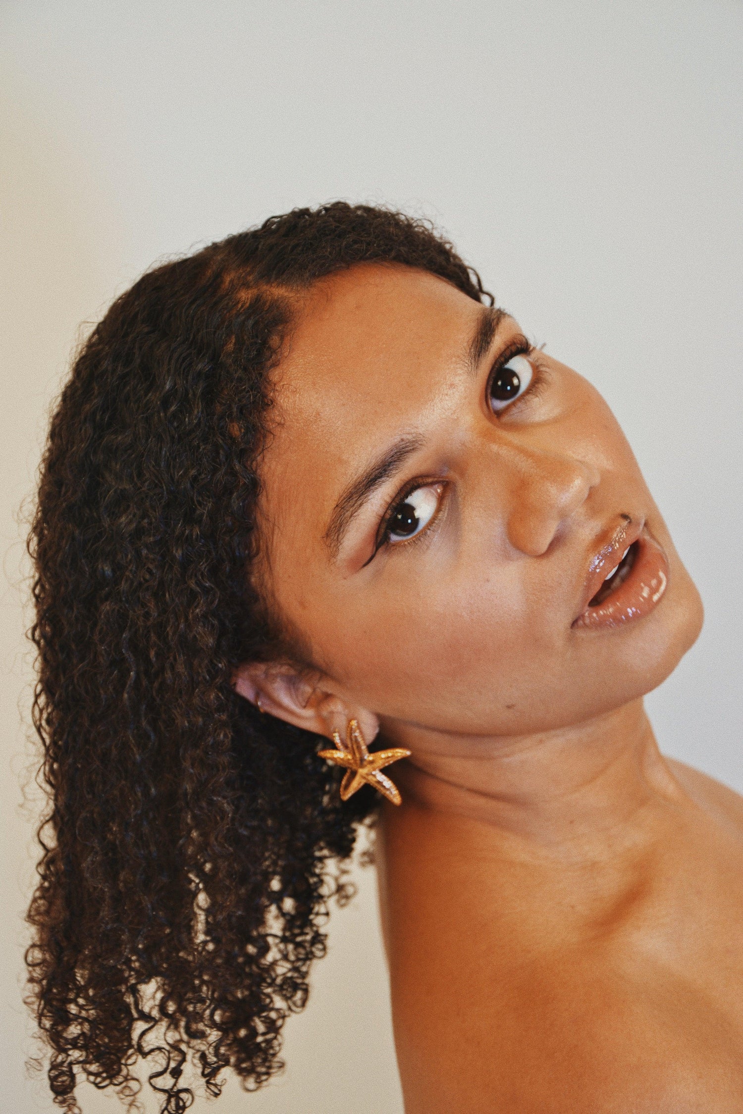Femme portant des boucles d’oreilles étoile de mer dorées, fond neutre, bijoux tendance