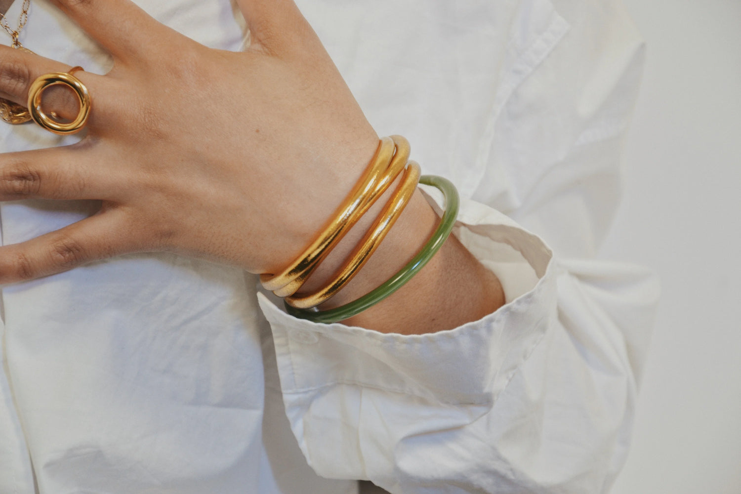 Bracelets joncs bouddhistes dorés et vert portés sur un poignet avec chemise blanche