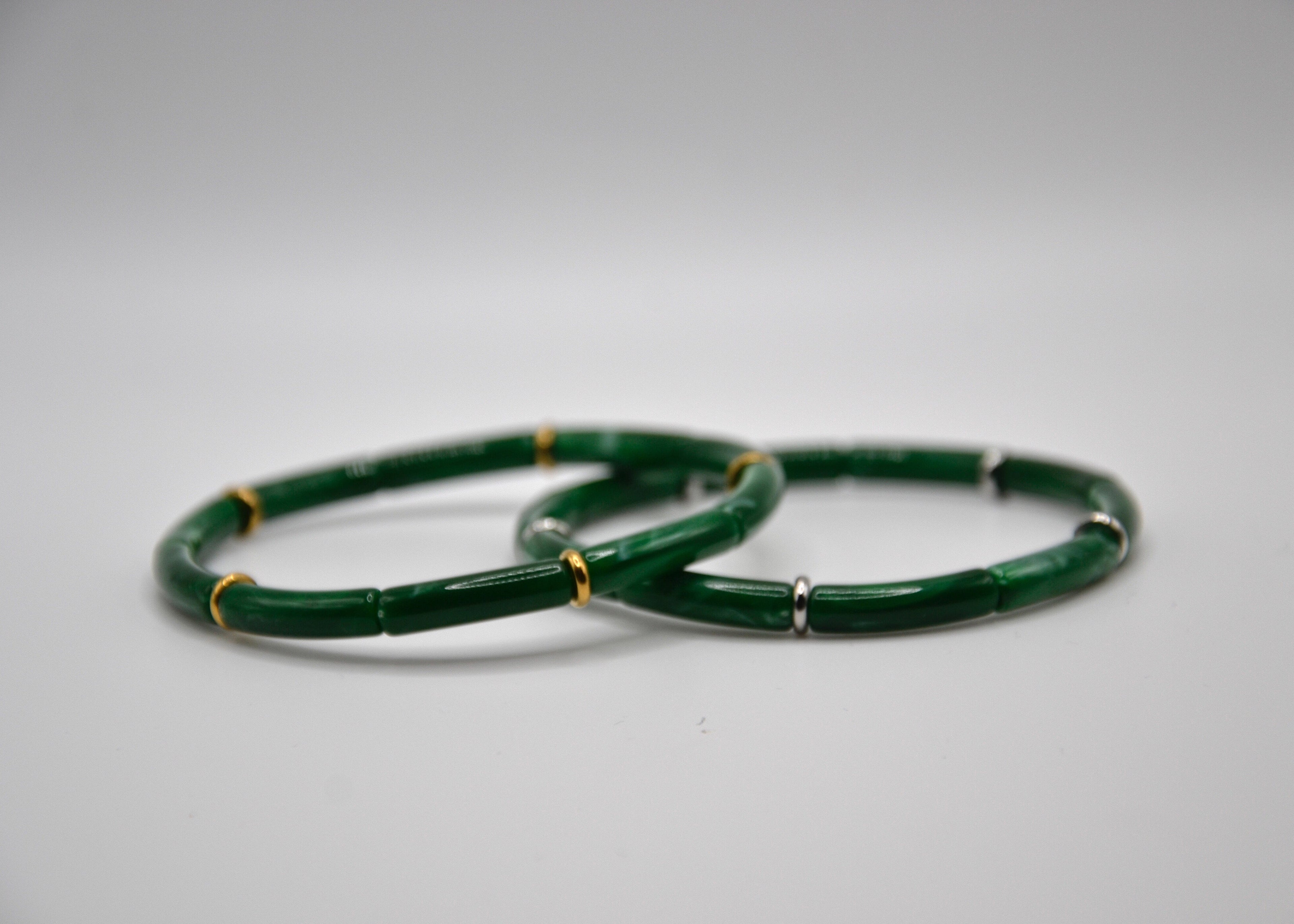 Deux bracelets en jade vert avec accents dorés et argentés sur fond blanc, bijoux élégants.