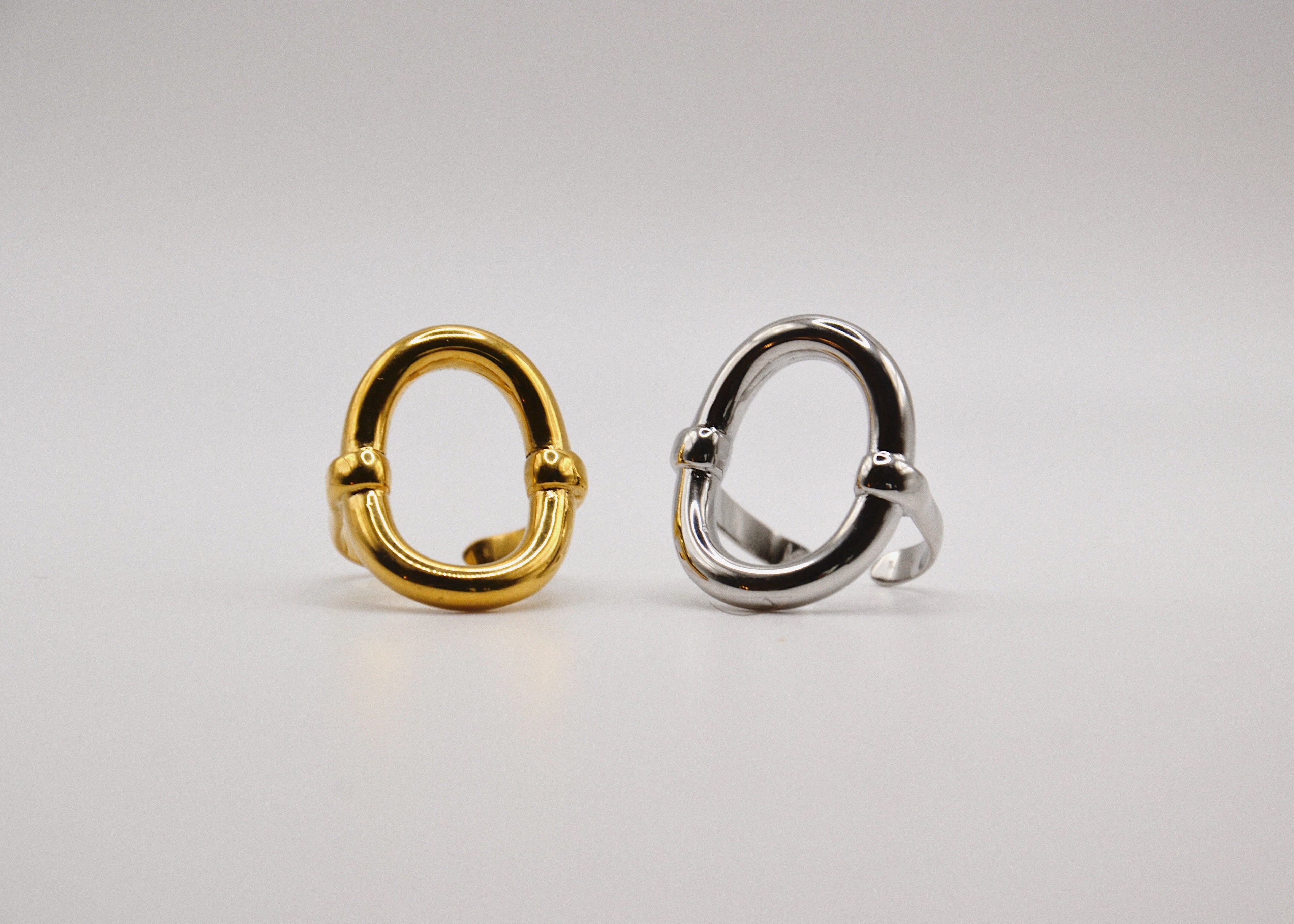Deux bagues ovales, une dorée et une argentée, sur fond blanc minimaliste.