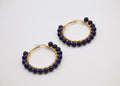 Boucles d’oreilles créoles dorées avec perles rondes bleu marine sur fond blanc