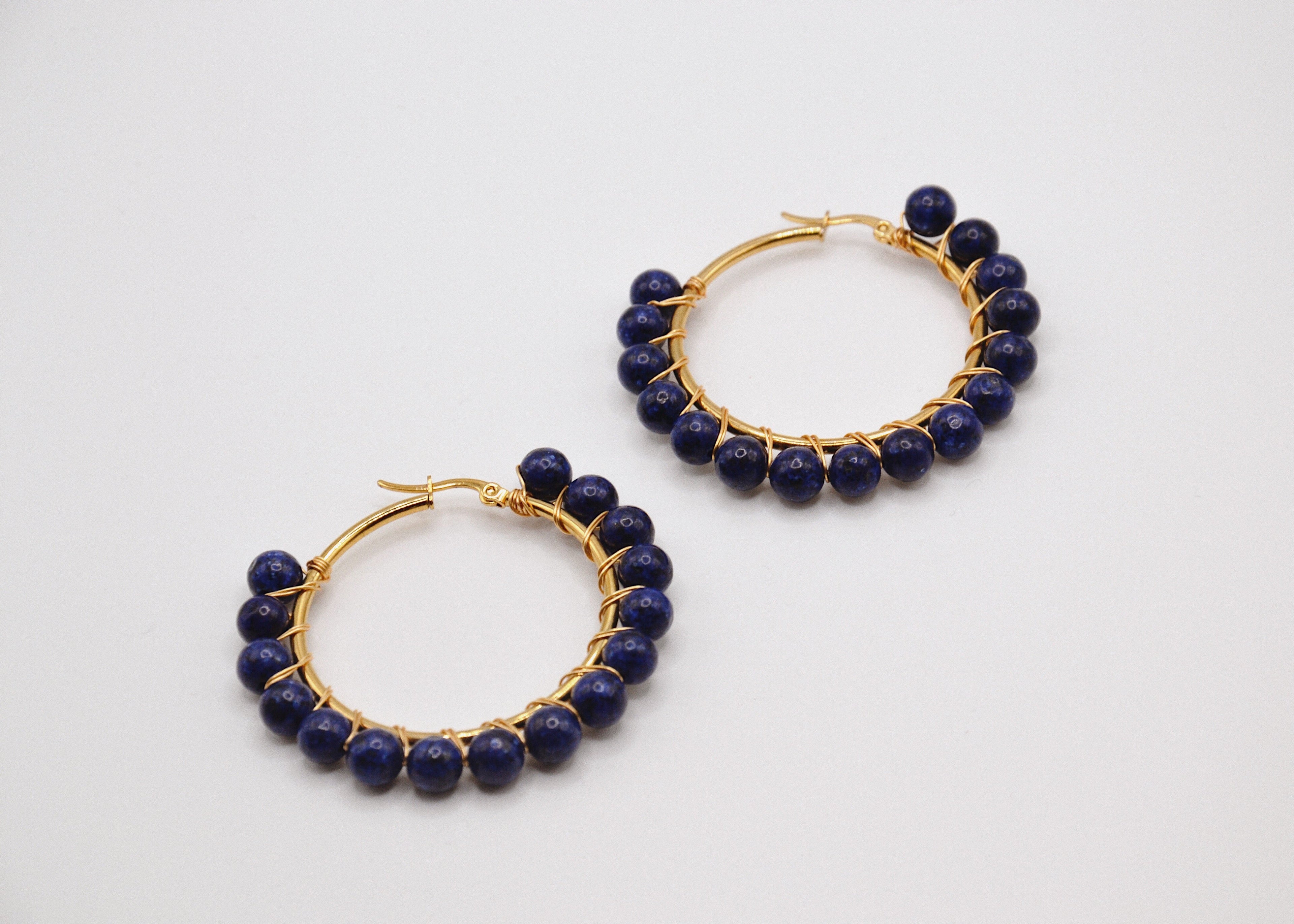 Boucles d’oreilles créoles dorées avec perles rondes bleu marine sur fond blanc