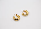 Boucles d’oreilles créoles dorées en forme de demi-cercle sur fond blanc minimaliste
