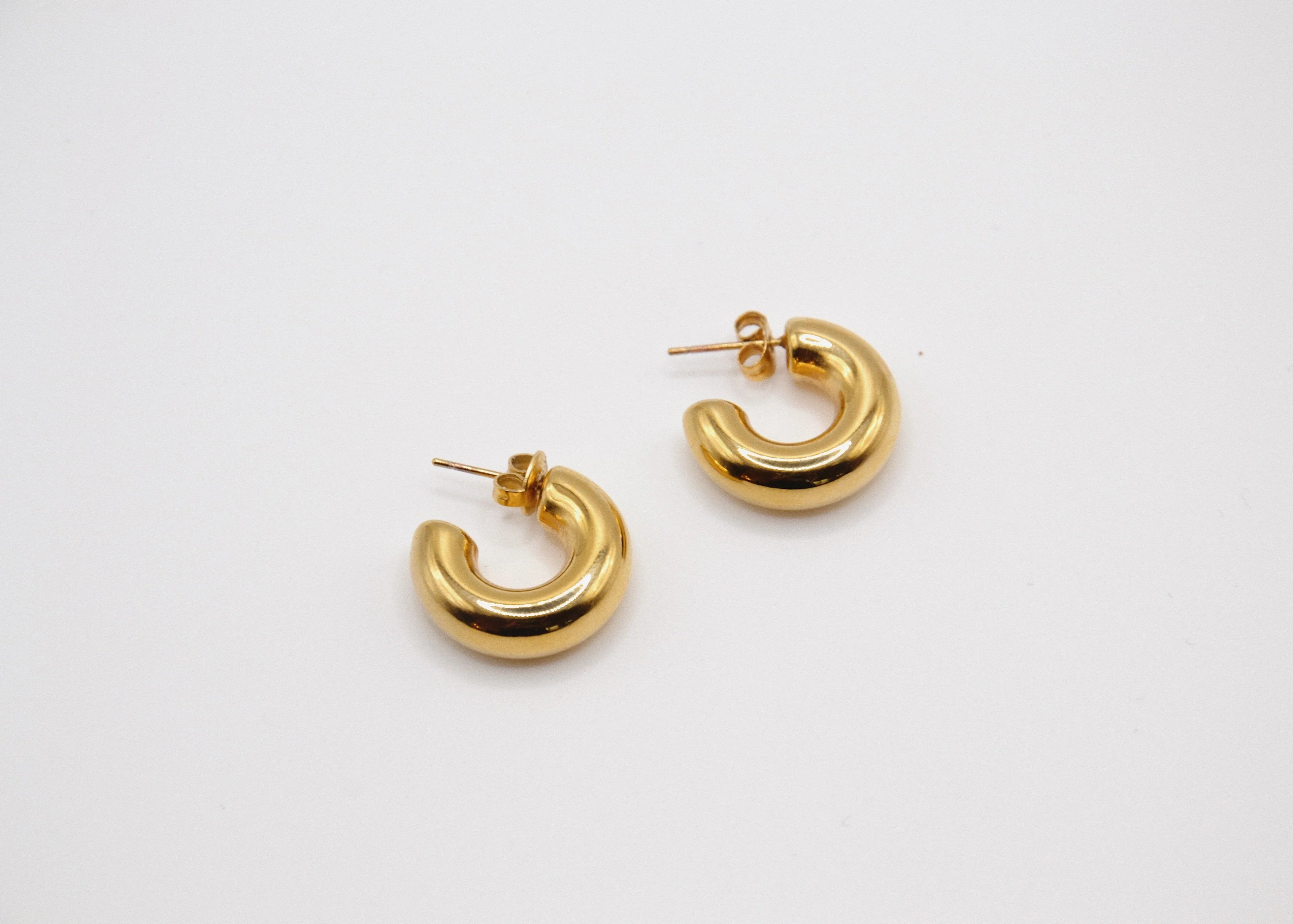 Boucles d’oreilles créoles dorées en forme de demi-cercle sur fond blanc minimaliste