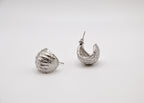 Boucles d'oreilles créoles argentées texturées posées sur fond blanc minimaliste