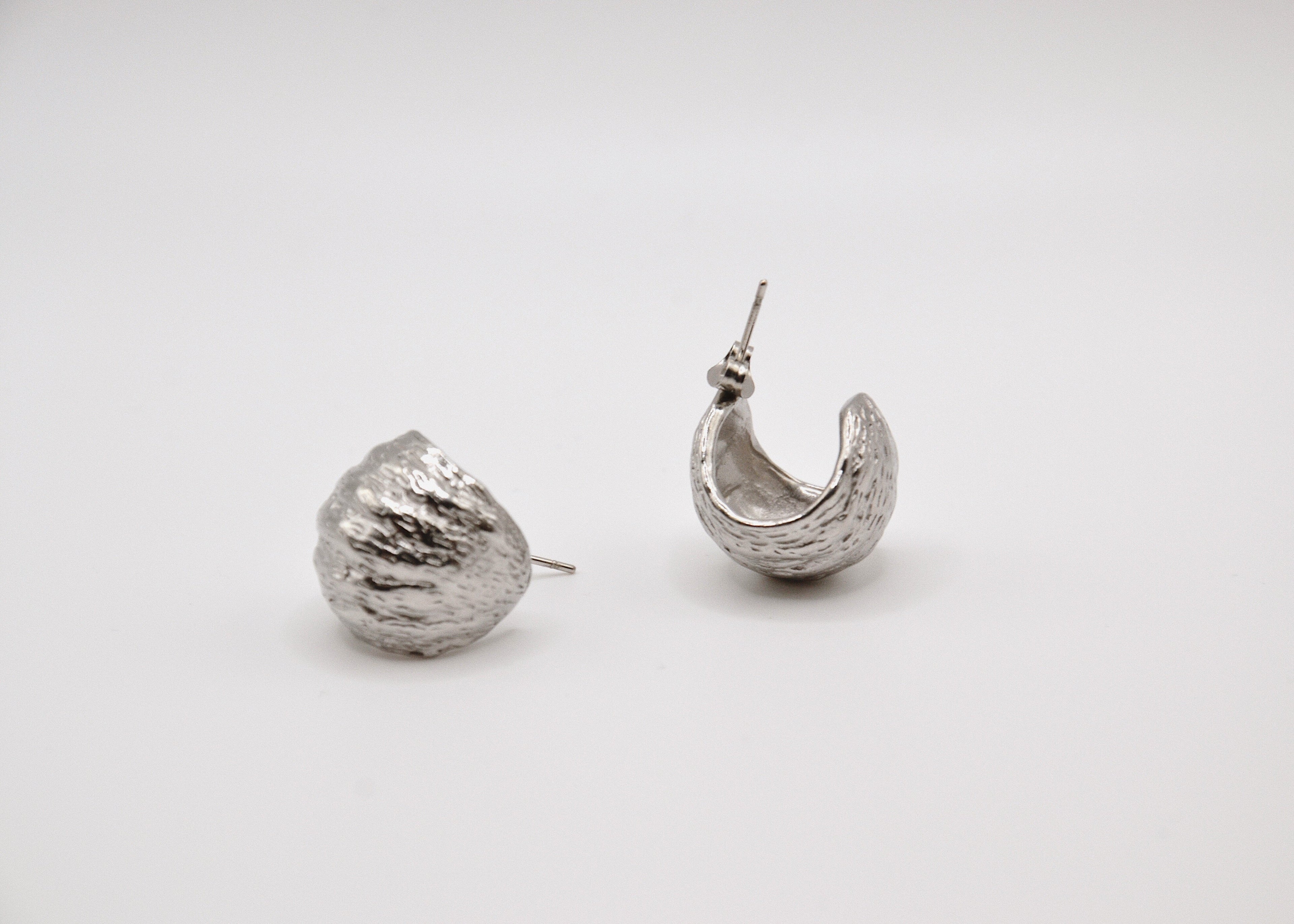 Boucles d'oreilles créoles argentées texturées posées sur fond blanc minimaliste