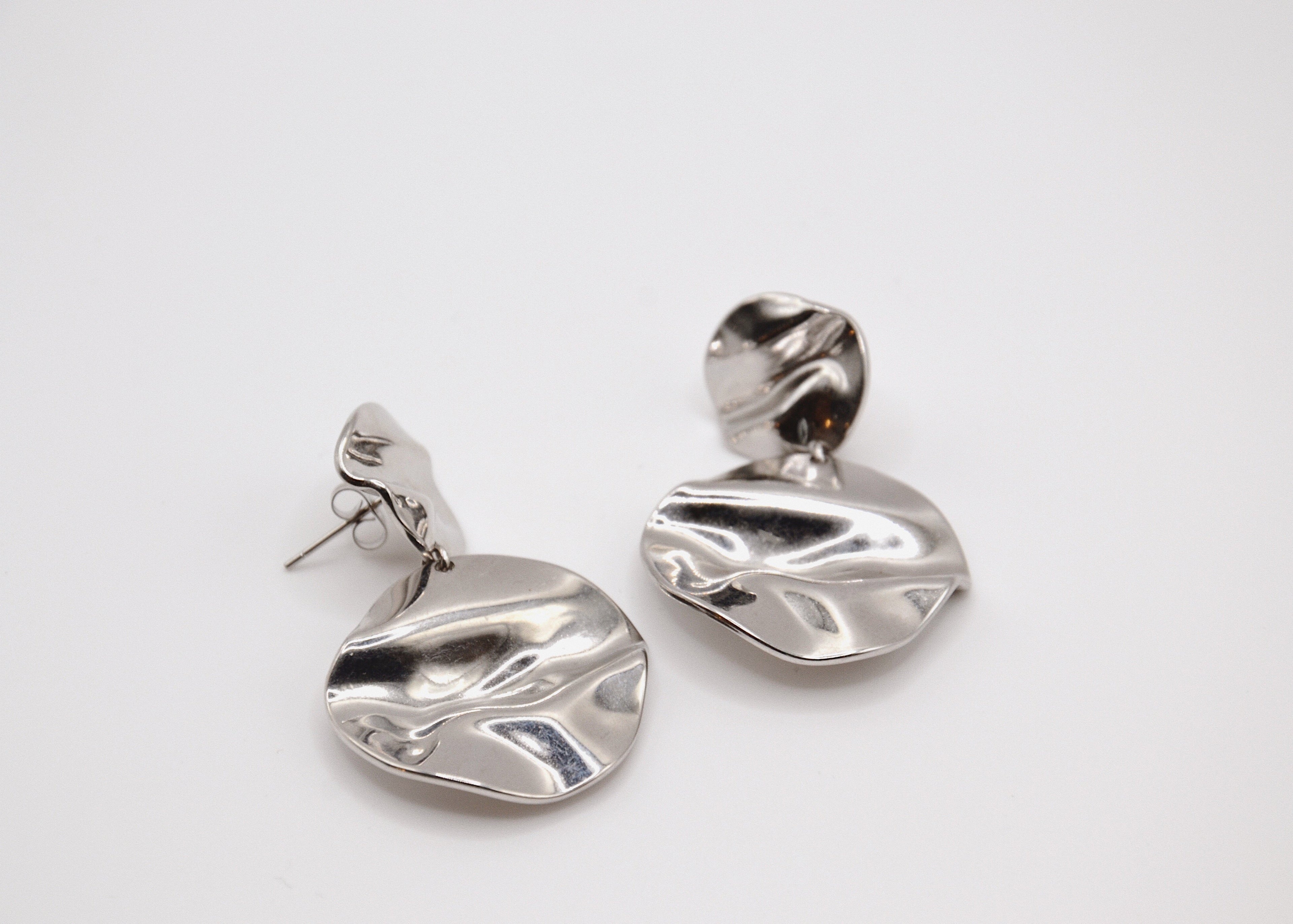 Boucles d’oreilles créoles argentées modernes effet ondulé sur fond blanc minimaliste