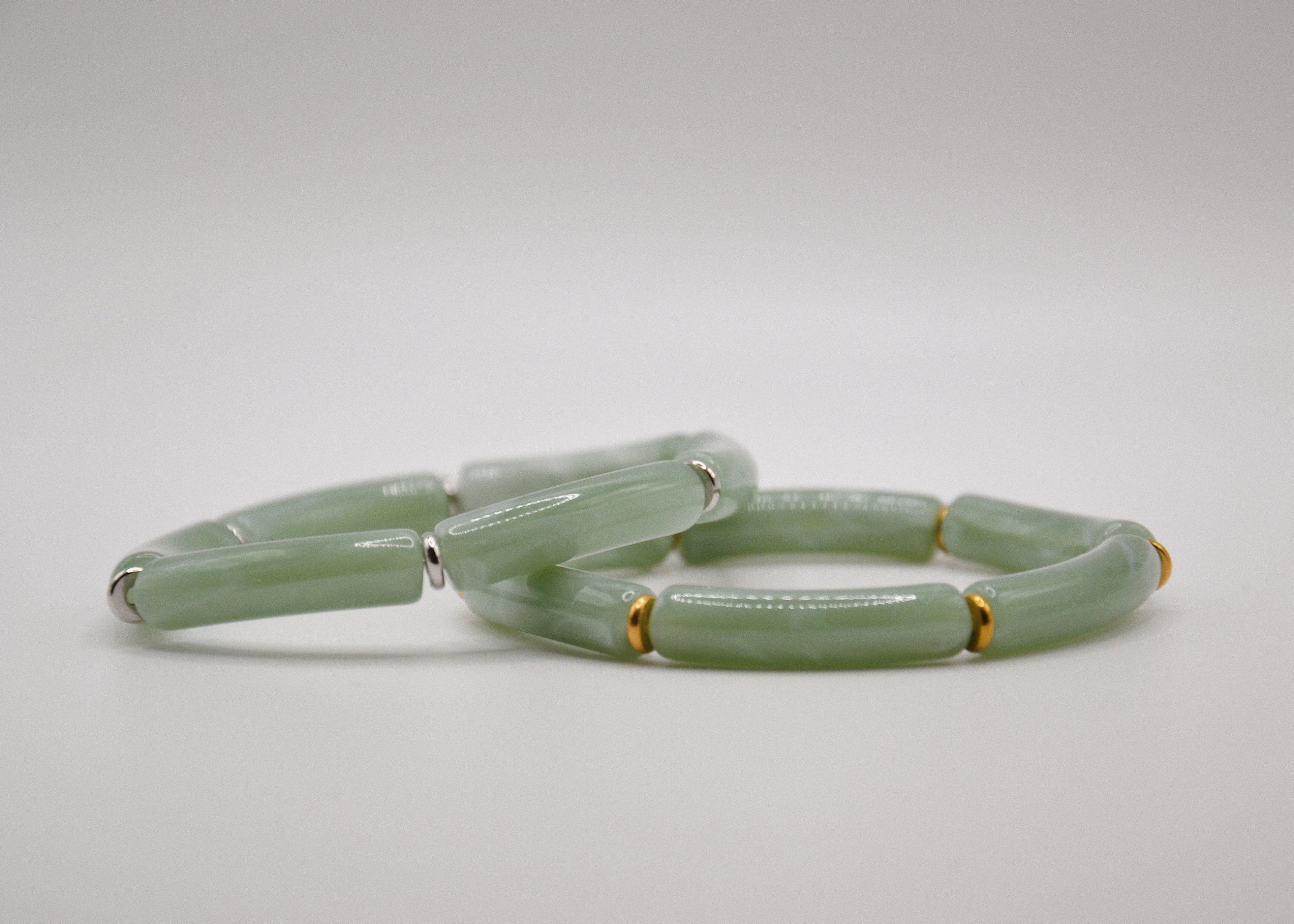 Bracelet en jade vert cylindrique avec séparateurs dorés sur fond blanc, bijou élégant.