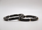 Bracelets en céramique noire avec accents dorés et argentés sur fond blanc, bijoux élégants
