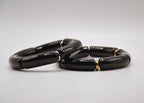 Bracelet moderne en céramique noire segmentée avec détails dorés sur fond blanc