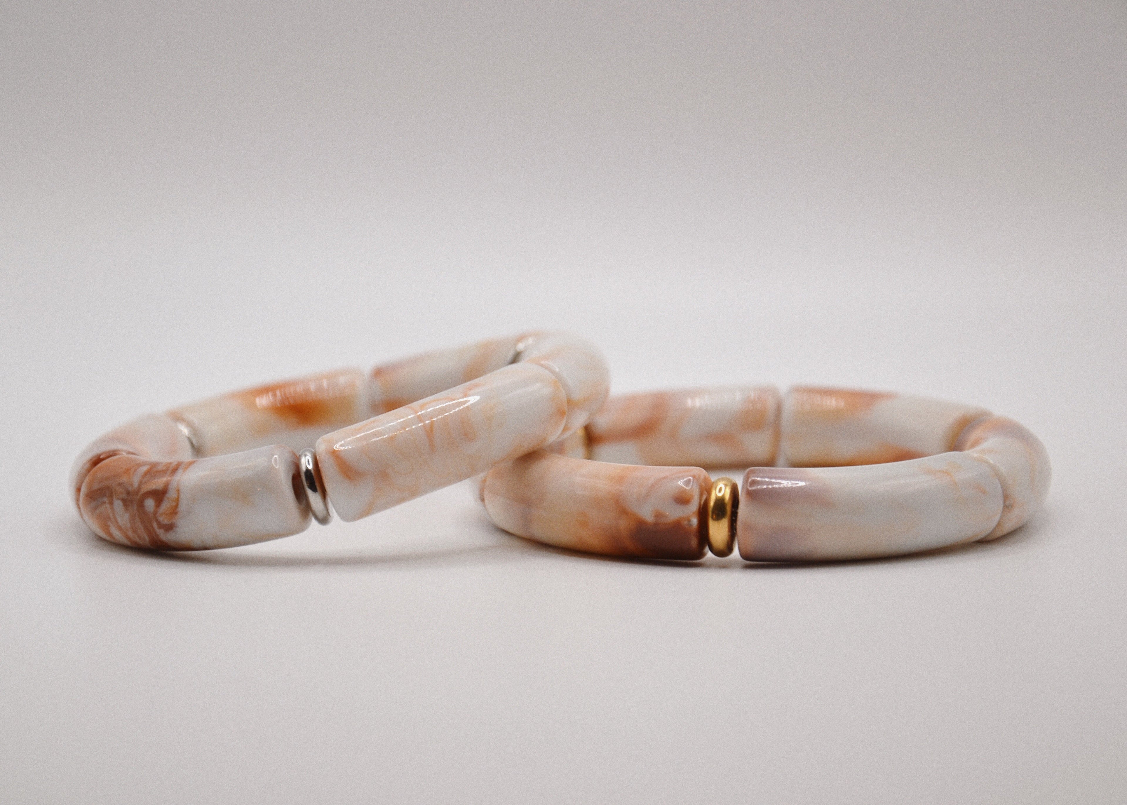 Bracelets en céramique marbrée blanc et beige avec accents dorés sur fond blanc