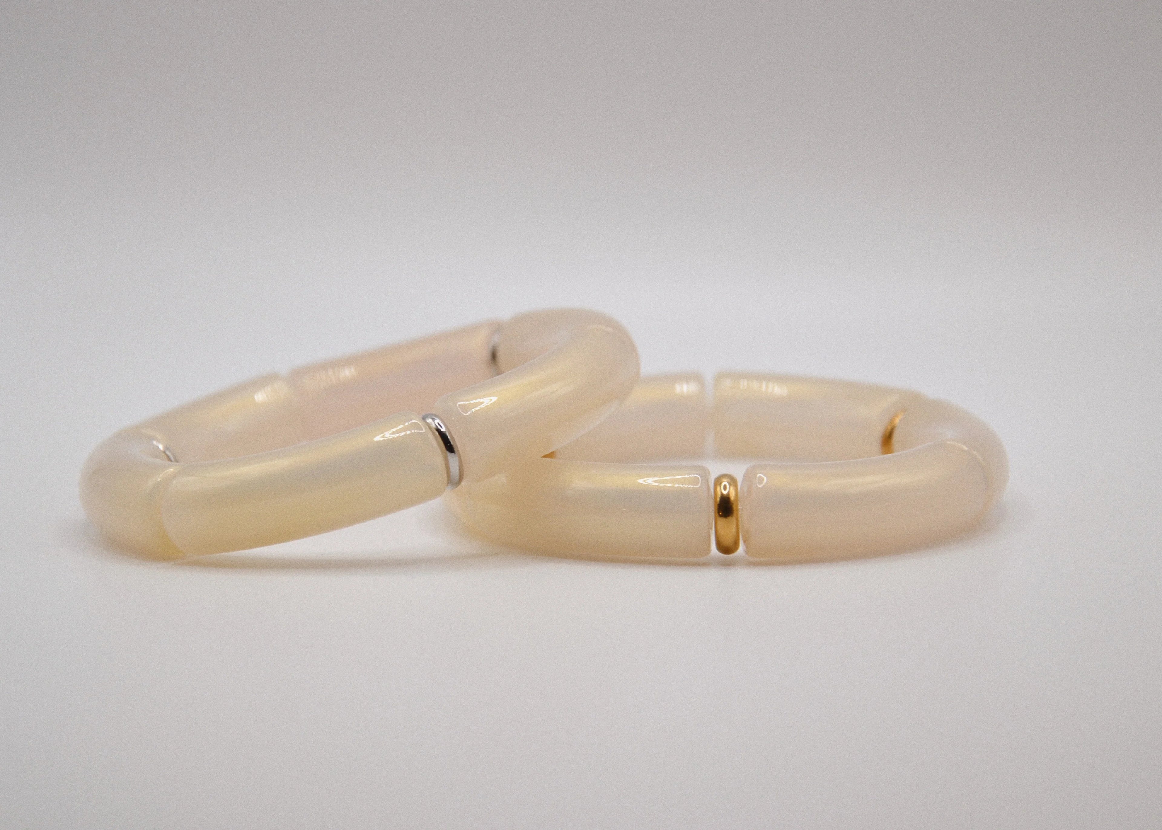Deux bracelets en résine beige crème, détails dorés et argentés, sur fond blanc.