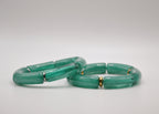 Deux bracelets verts en résine avec anneaux dorés, posés sur fond blanc, bijoux modernes.