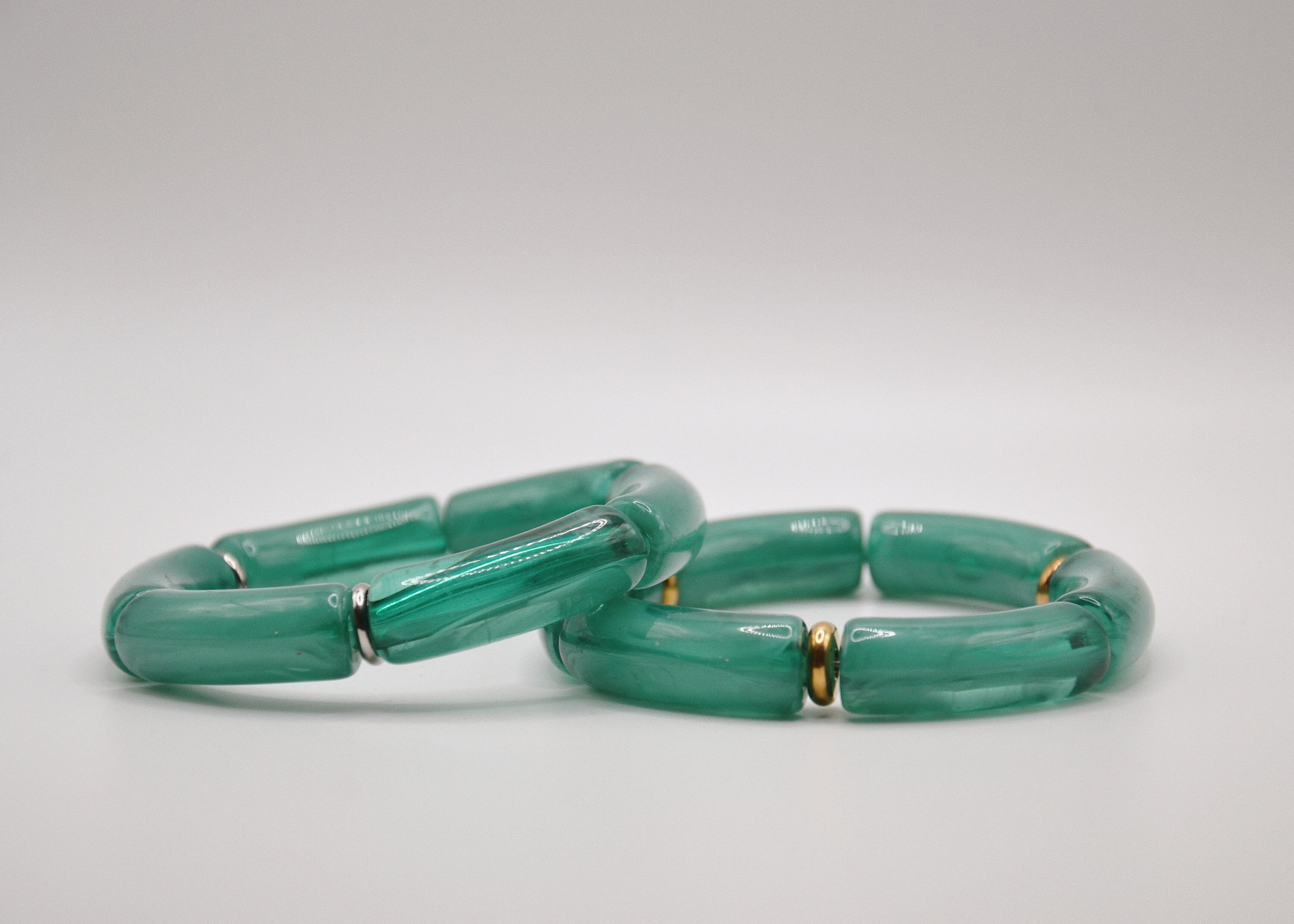 Deux bracelets verts en résine avec anneaux dorés, posés sur fond blanc, bijoux modernes.