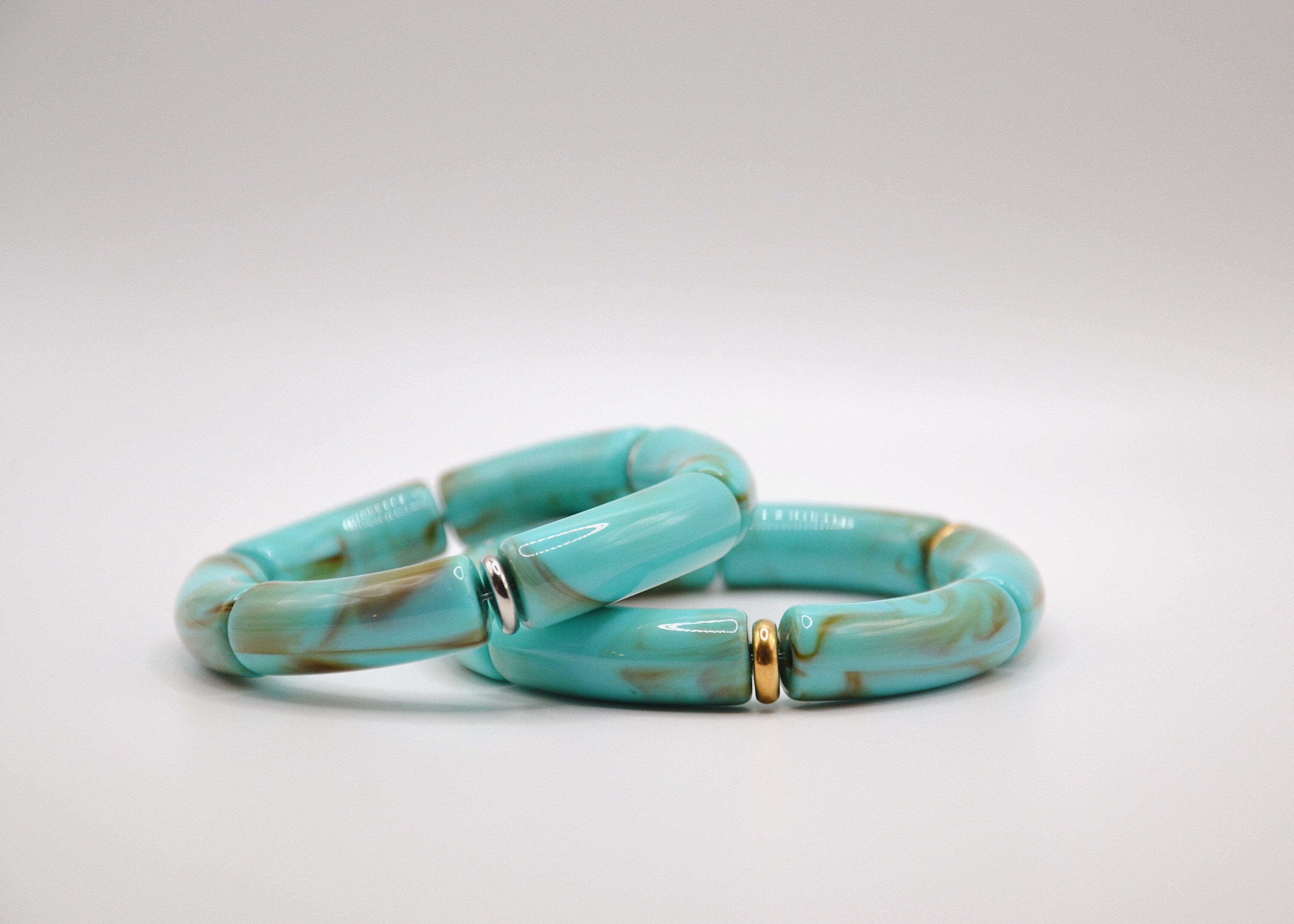 Bracelet en résine turquoise et marron avec accents dorés et argentés sur fond blanc