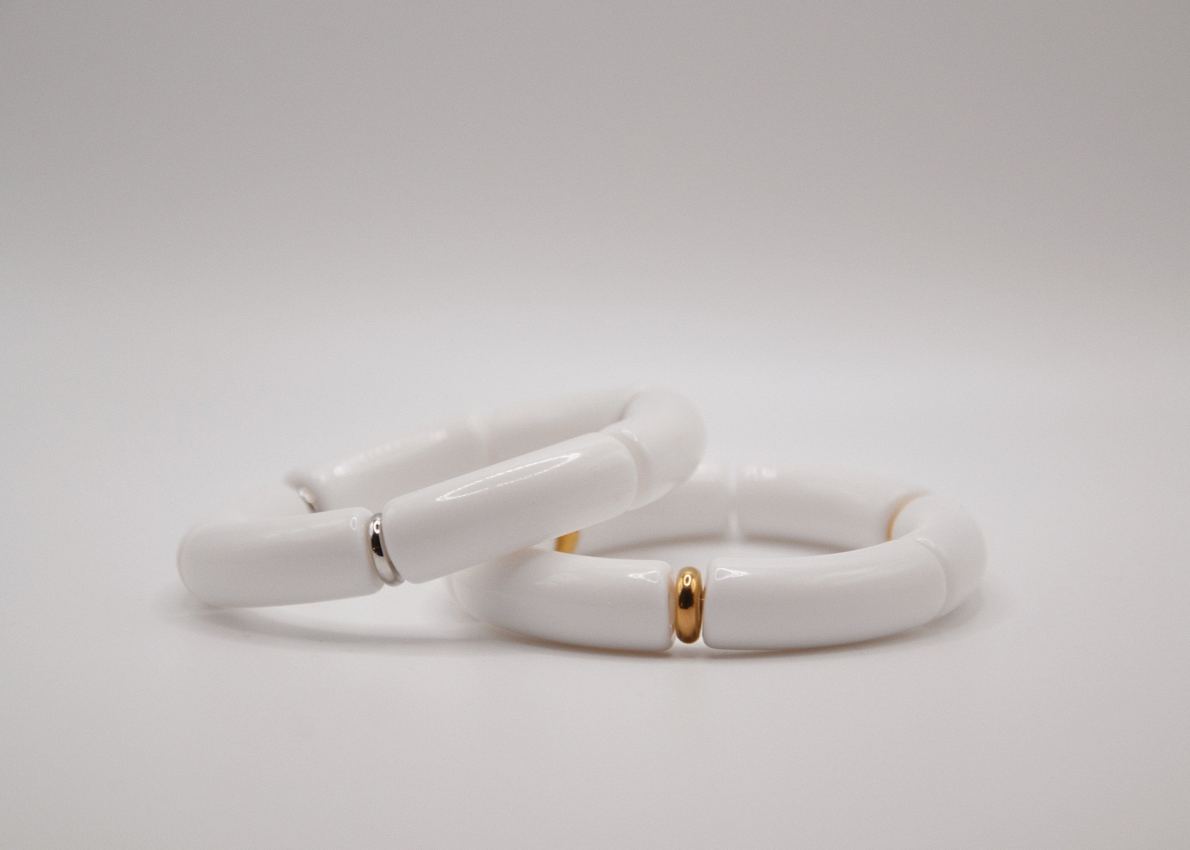 Deux bracelets céramique blanche avec accents dorés et argentés sur fond blanc minimaliste