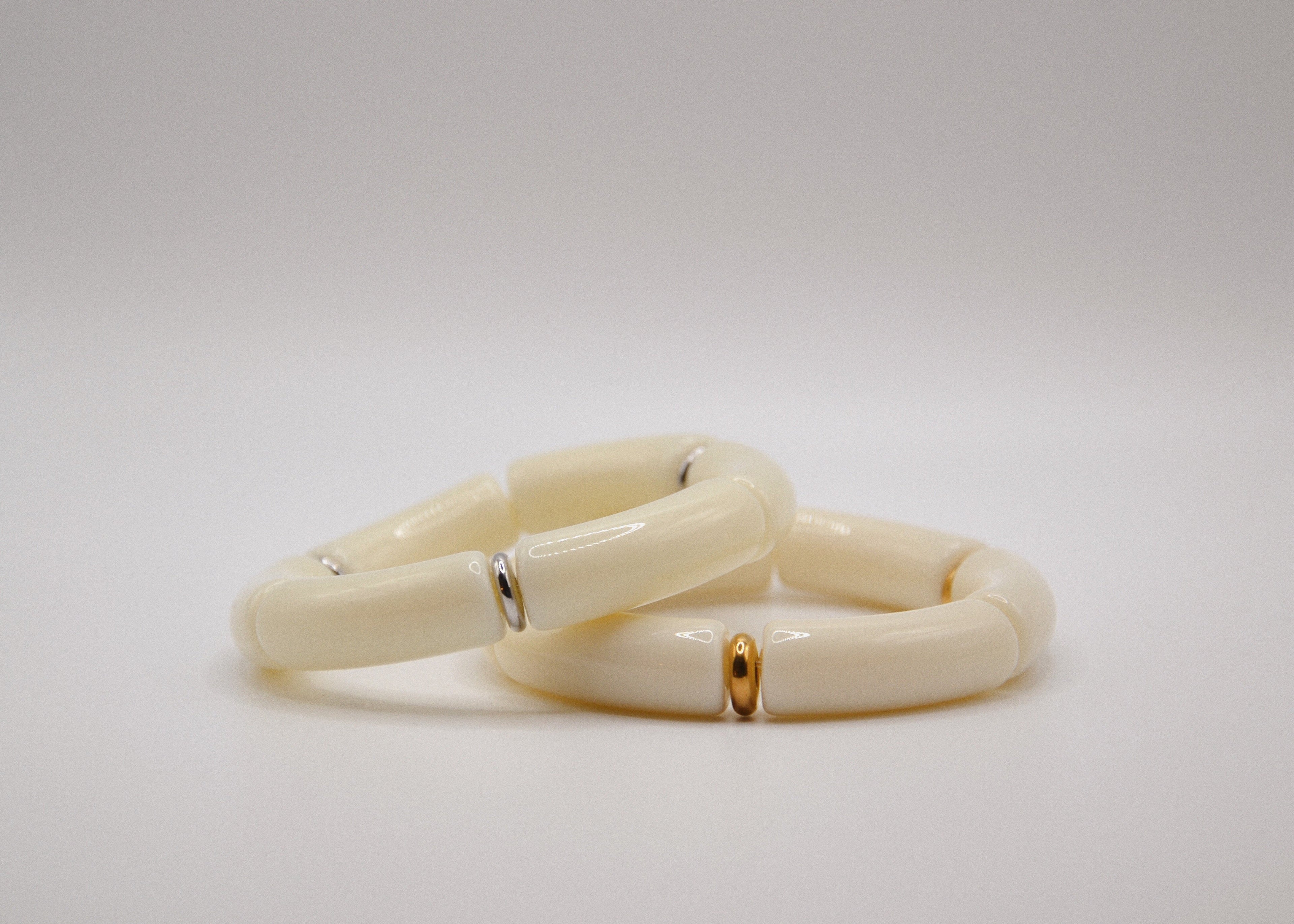 Bracelets en résine ivoire sur fond blanc, détails dorés et argentés, bijoux modernes élégants