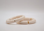 Deux bracelets céramique blanc cassé avec accents dorés et argentés sur fond blanc minimaliste