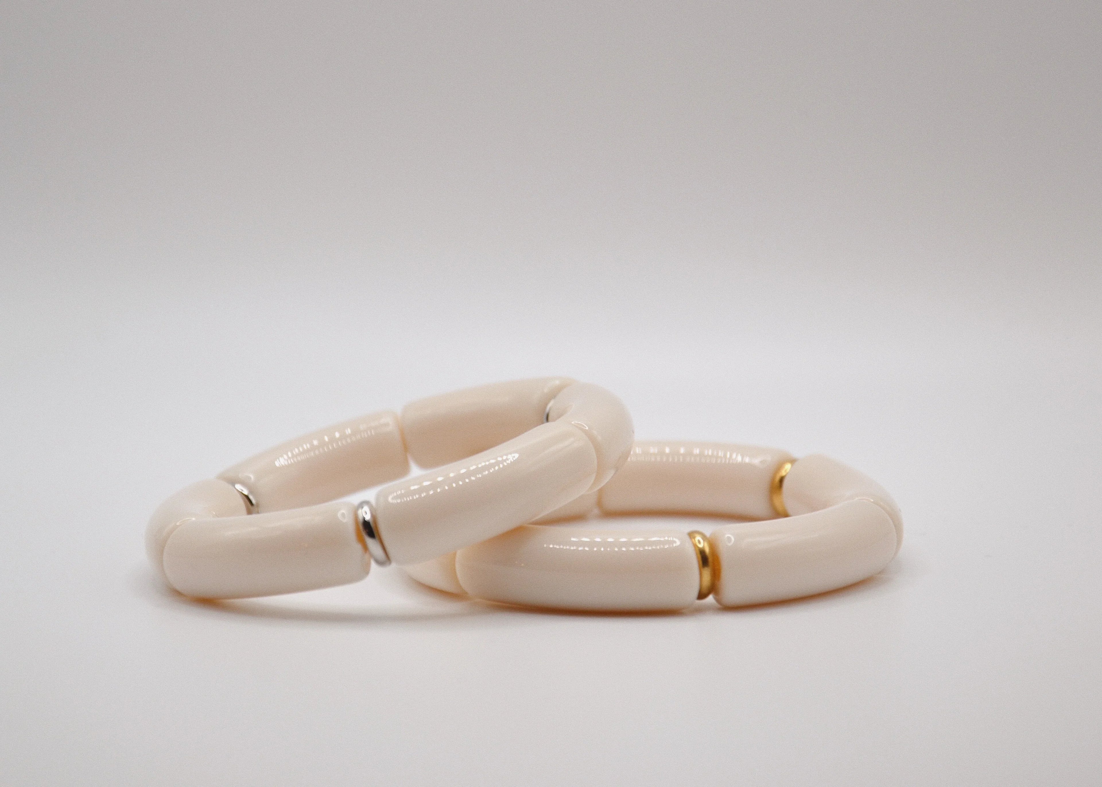 Deux bracelets céramique blanc cassé avec accents dorés et argentés sur fond blanc minimaliste