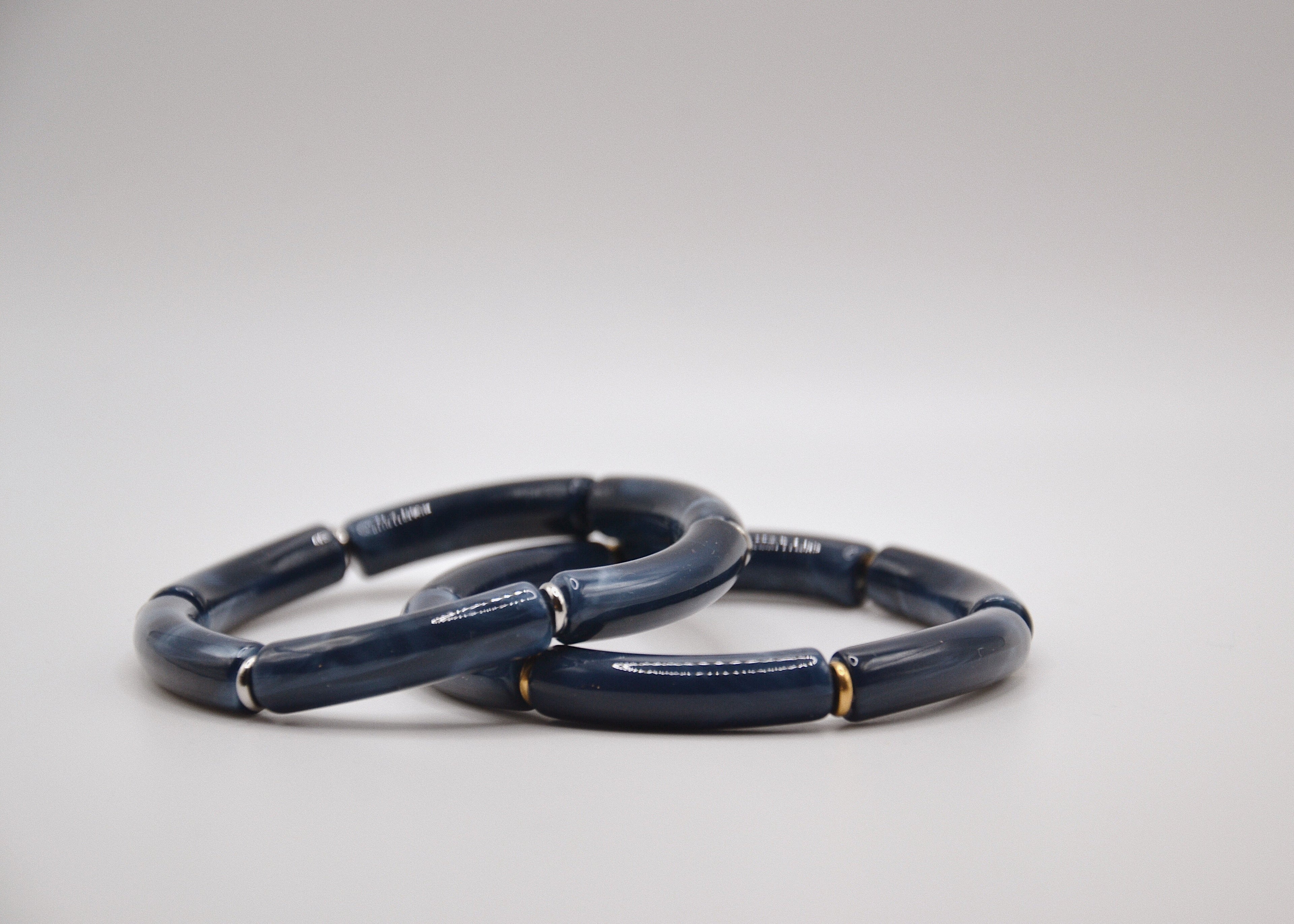 Deux bracelets bleu marine en résine à segments, fond blanc, style minimaliste élégant
