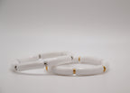 Bracelets blancs en céramique avec accents dorés et argentés sur fond blanc minimaliste