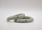 Bracelets épais gris clair avec détails dorés et argentés sur fond blanc, bijou moderne.