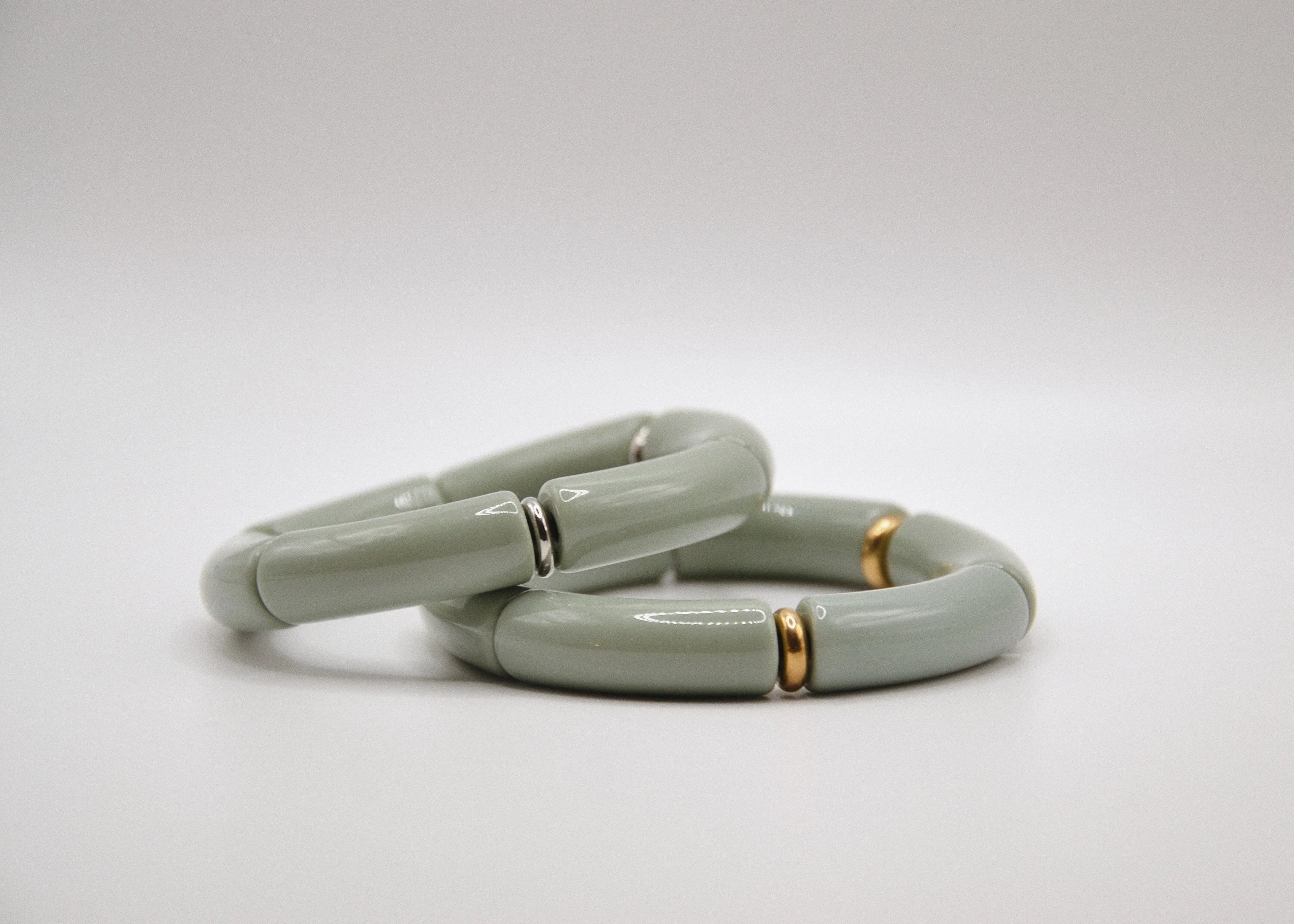 Bracelets épais gris clair avec détails dorés et argentés sur fond blanc, bijou moderne.