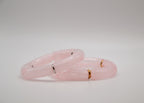 Bracelets en résine rose avec anneaux dorés et argentés sur fond blanc minimaliste