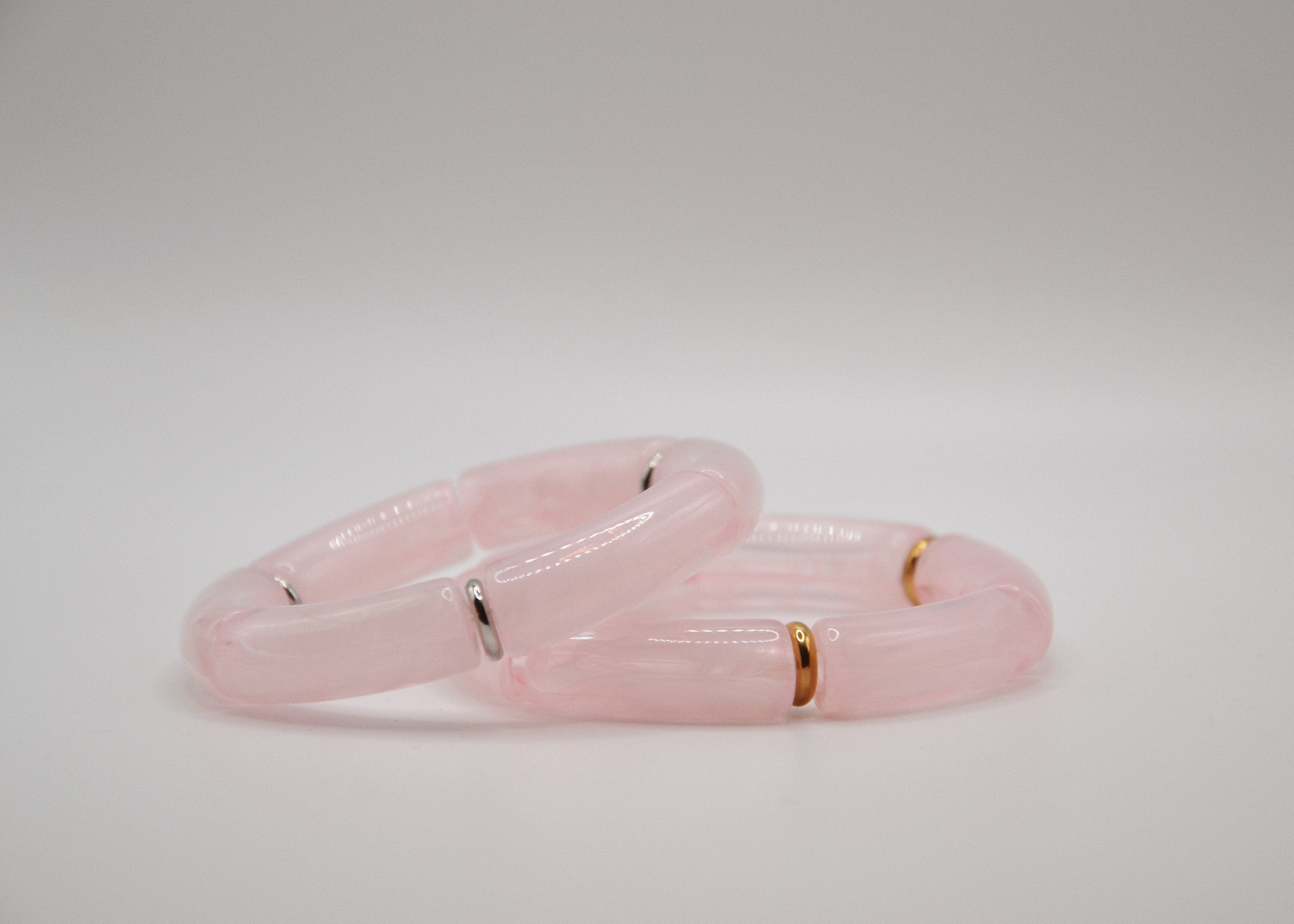 Bracelets en résine rose avec anneaux dorés et argentés sur fond blanc minimaliste