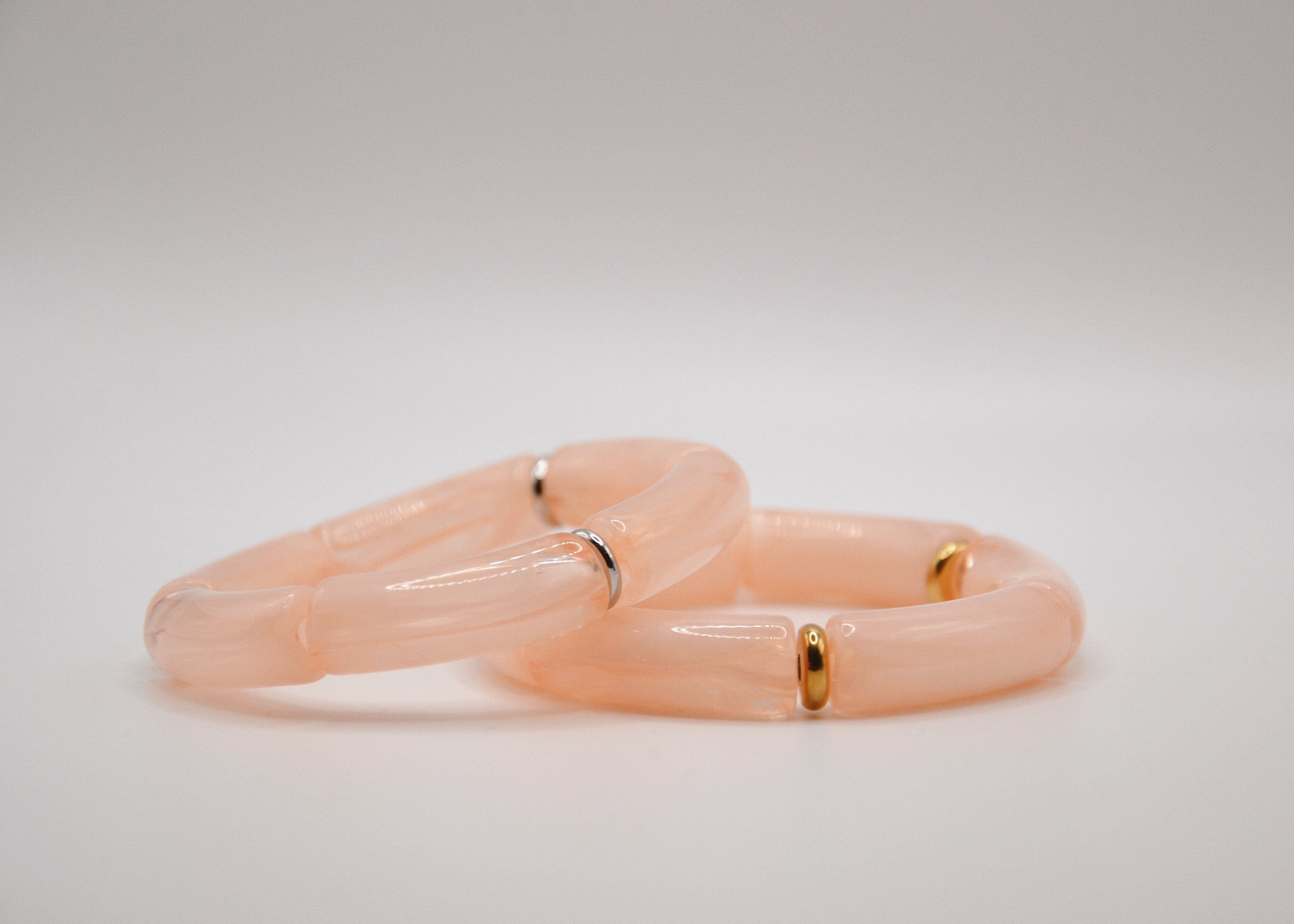 Deux bracelets transparents rose clair avec anneaux dorés et argentés sur fond blanc