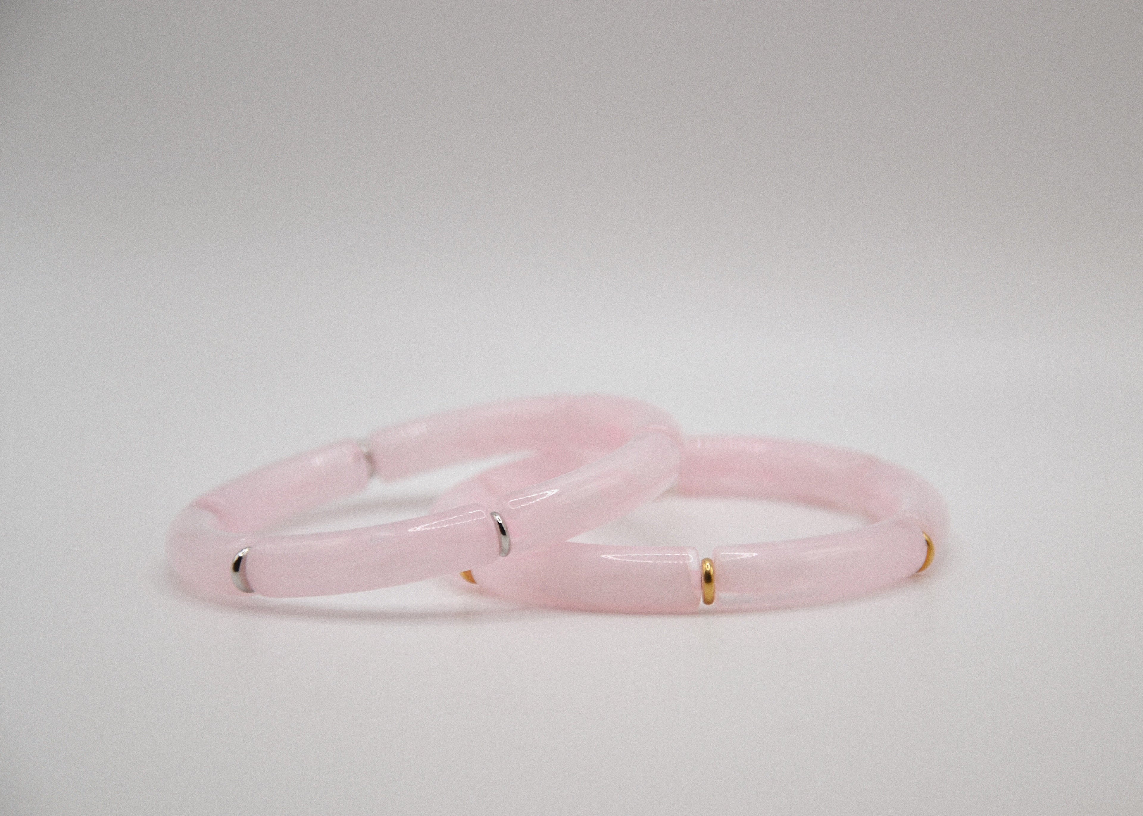 Deux bracelets en jade rose avec détails dorés et argentés sur fond blanc minimaliste