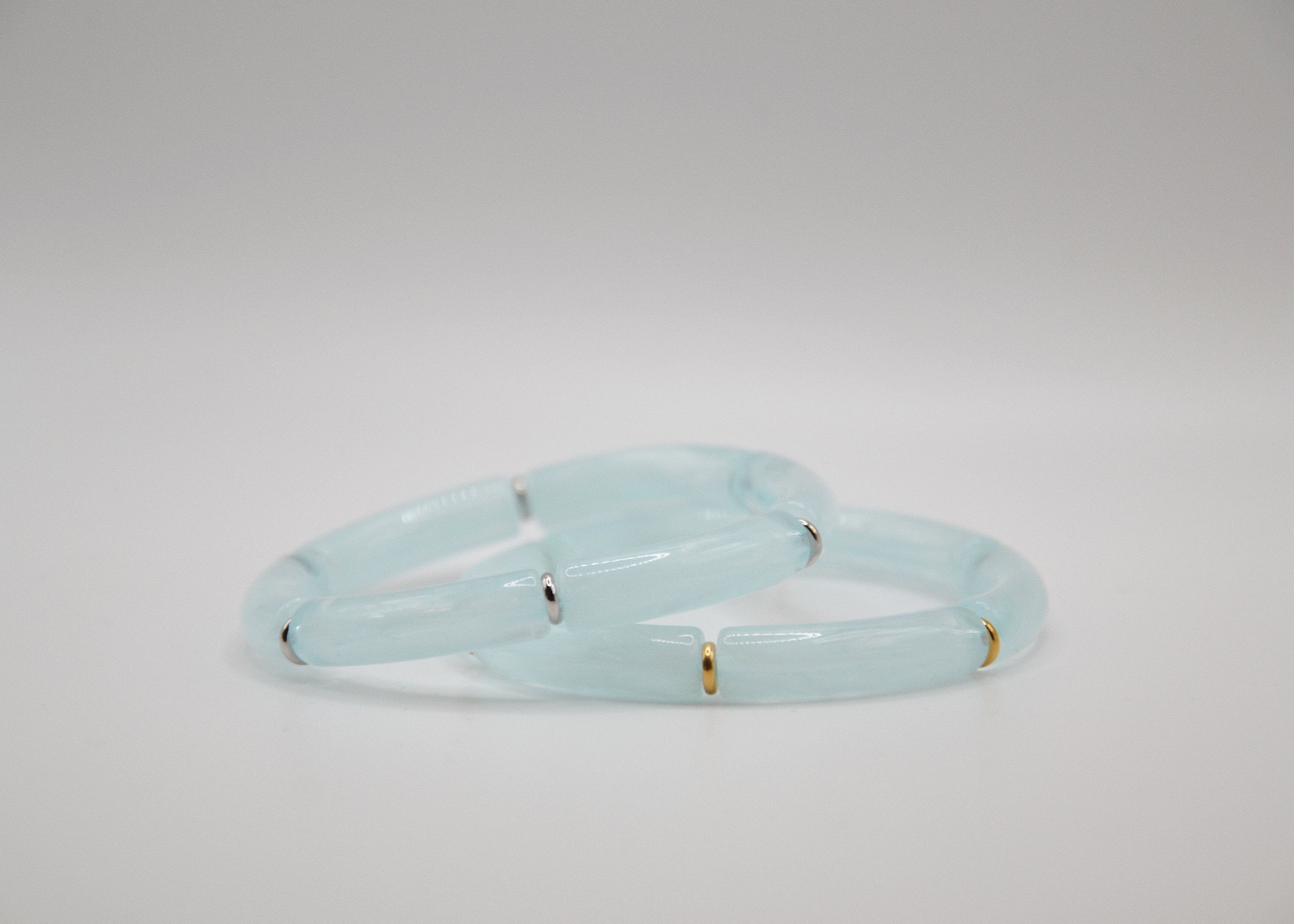Bracelets en jade bleu pâle avec accents dorés et argentés sur fond blanc minimaliste