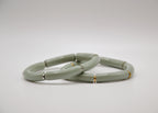 Deux bracelets en céramique vert sauge avec détails dorés et argentés sur fond blanc.