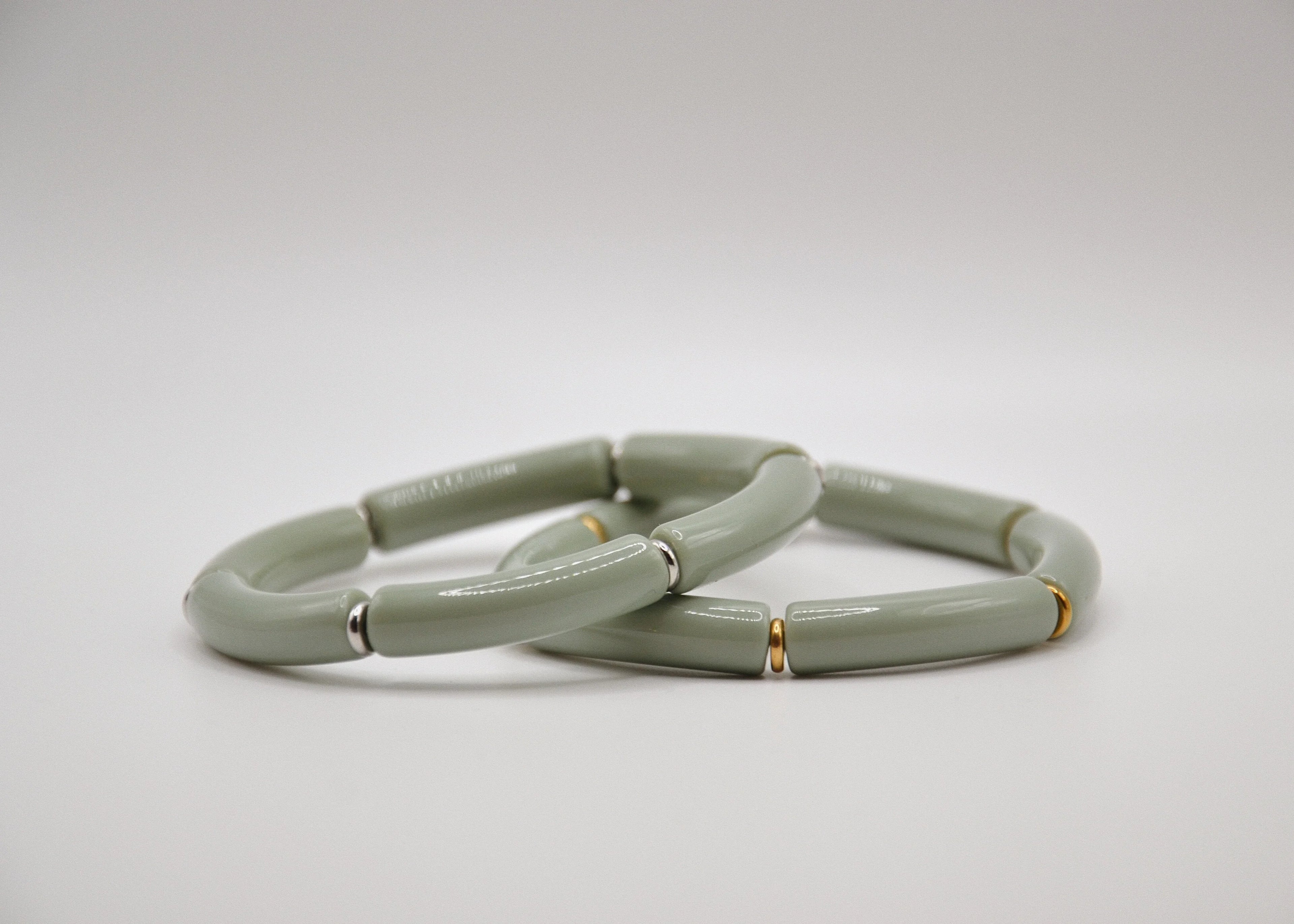 Deux bracelets en céramique vert sauge avec détails dorés et argentés sur fond blanc.