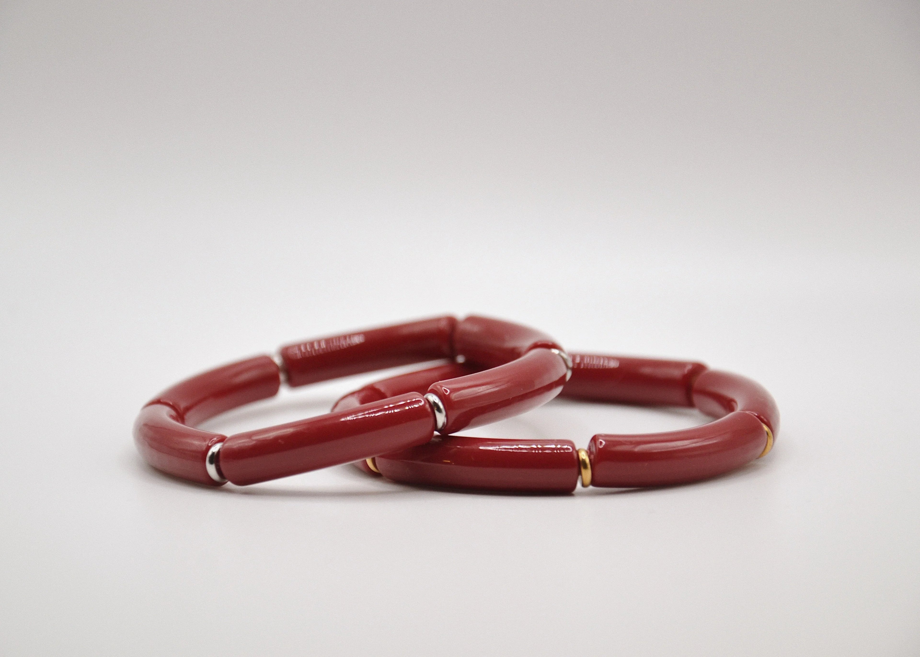 Bracelets rouges en résine avec détails dorés et argentés sur fond blanc, bijou moderne