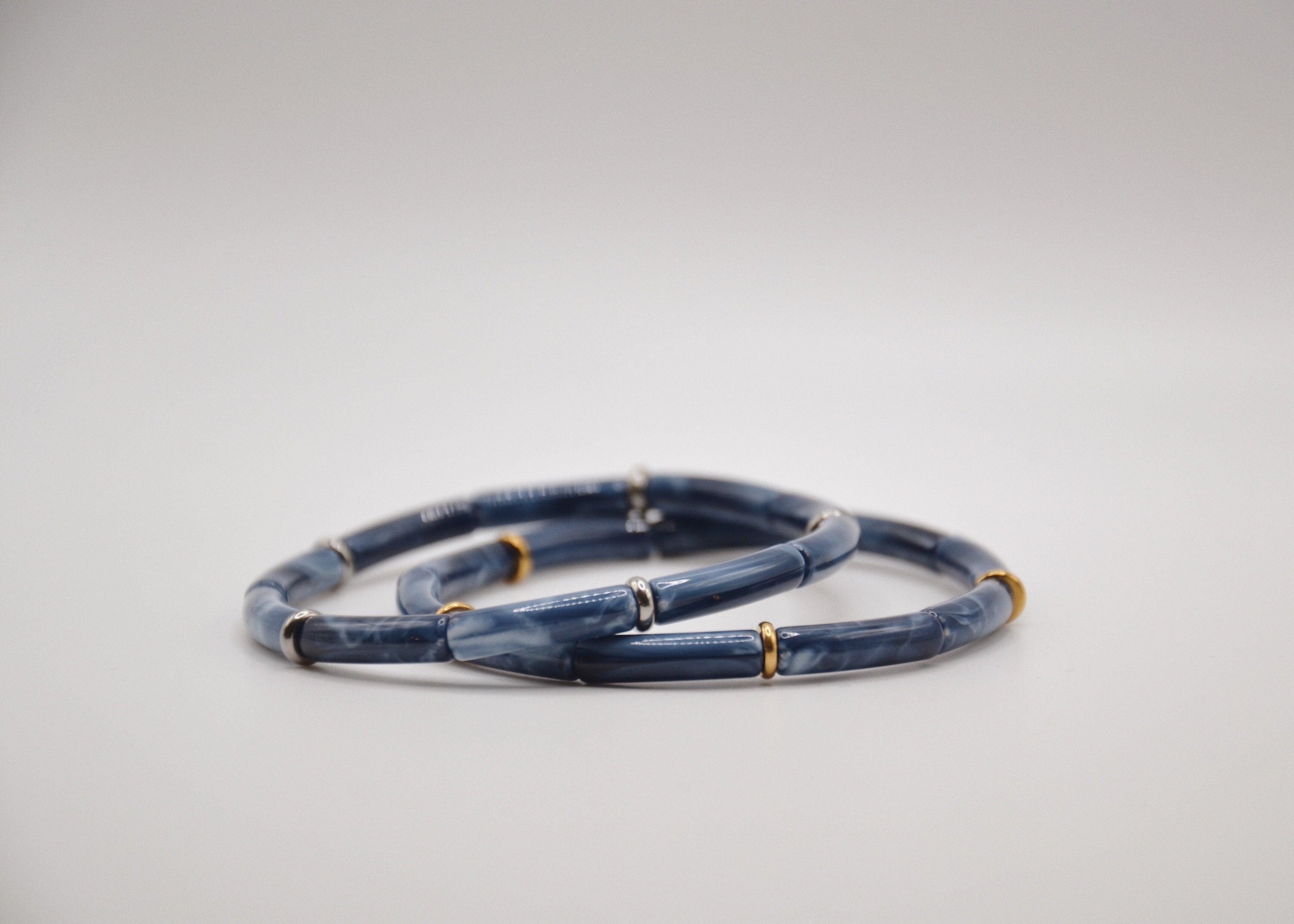 Bracelets bleus effet marbré avec anneaux dorés et argentés sur fond blanc, bijou moderne.