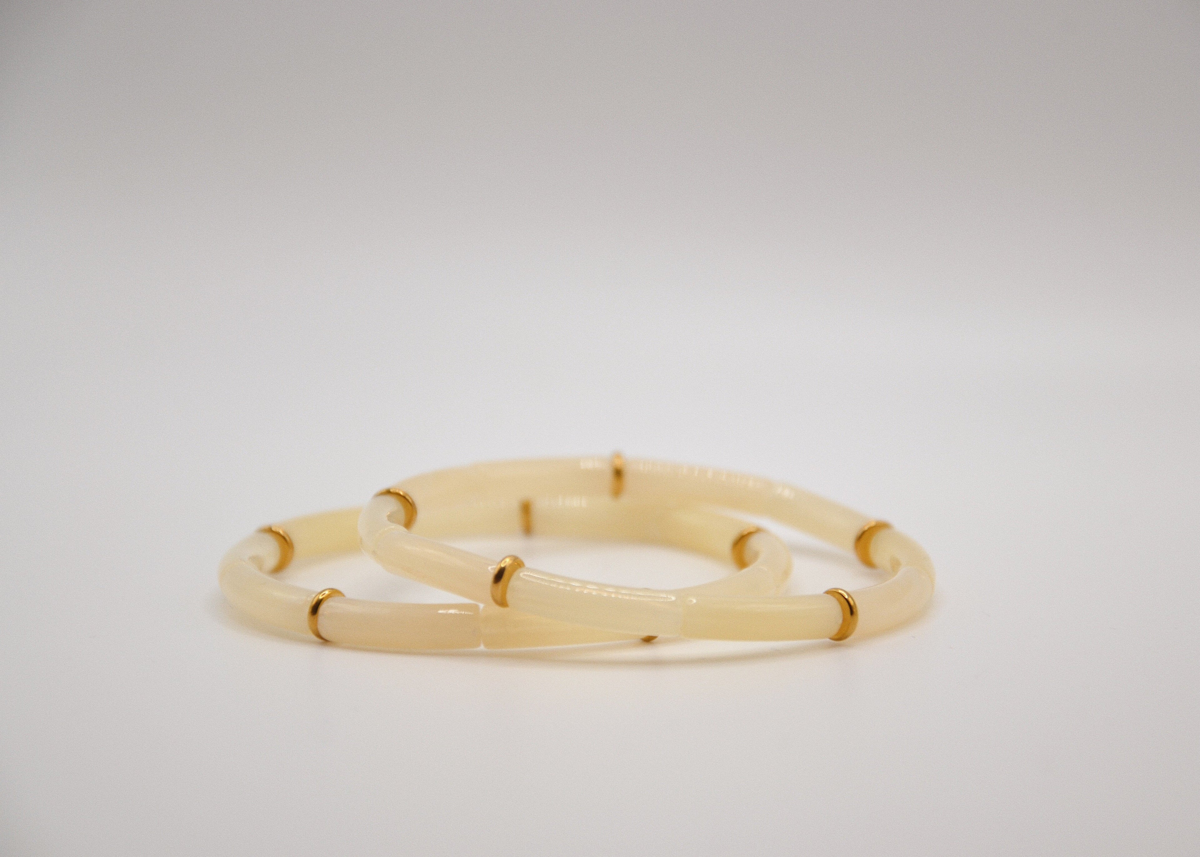 Deux bracelets en résine beige avec anneaux dorés sur fond blanc, bijoux minimalistes élégants