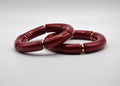 Deux bracelets rouges segmentés avec anneaux dorés et argentés sur fond blanc, bijoux tendance.