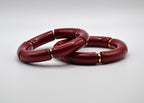 Deux bracelets rouges segmentés avec anneaux dorés et argentés sur fond blanc, bijoux tendance.