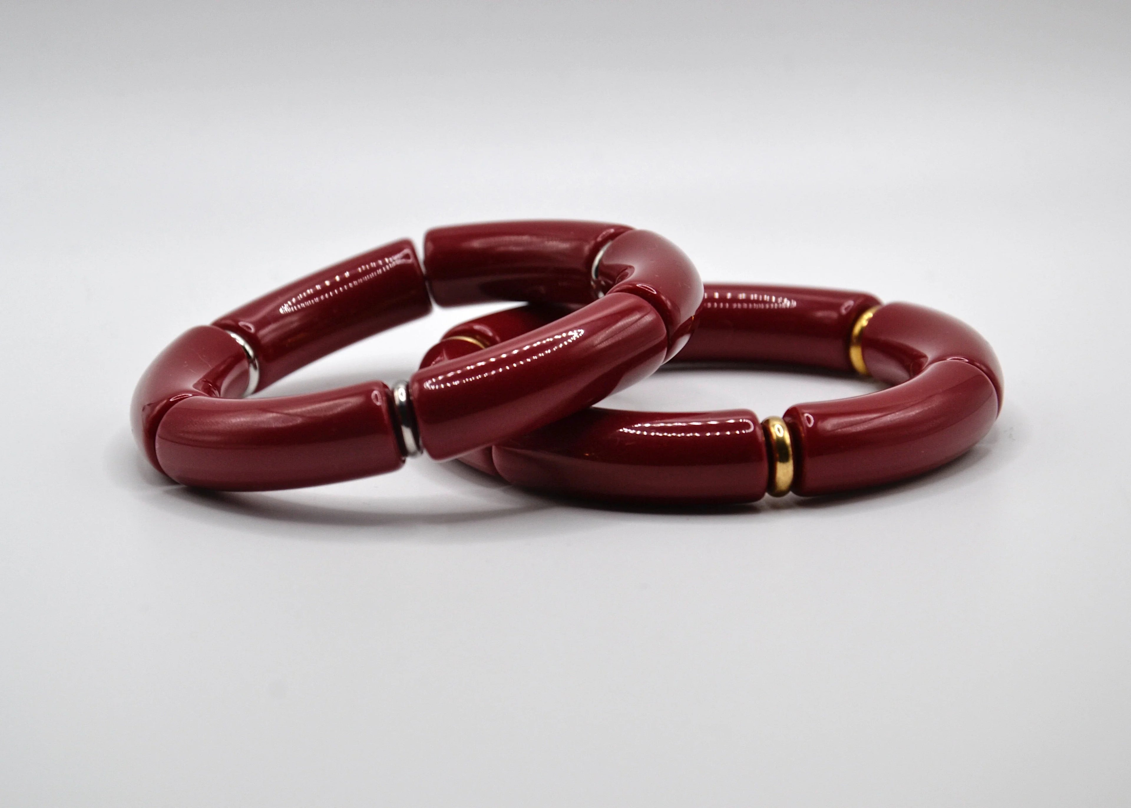 Deux bracelets rouges segmentés avec anneaux dorés et argentés sur fond blanc, bijoux tendance.