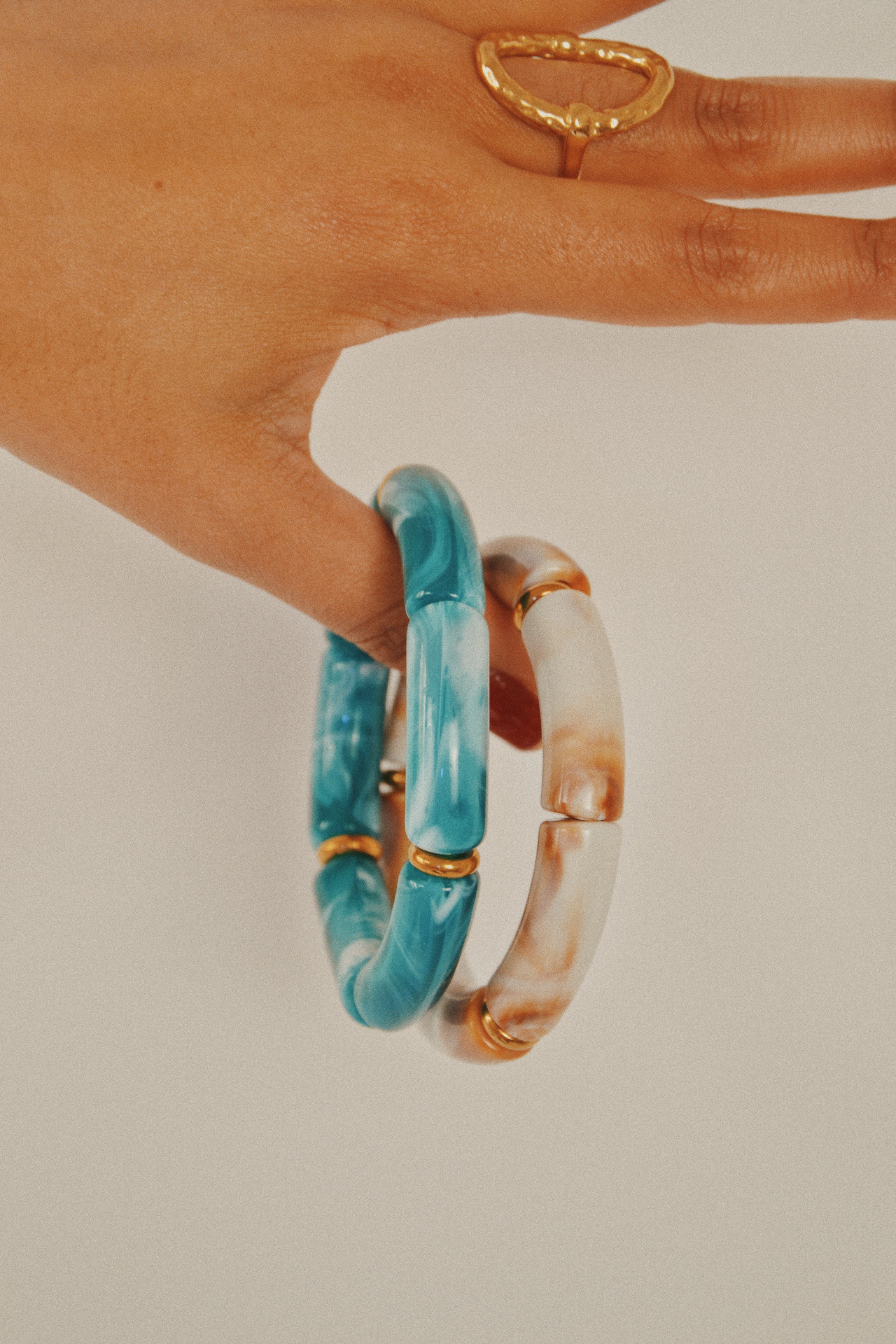 Main posant deux bracelets bambou bleu et beige marbrés avec anneaux dorés, bague dorée