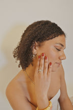 Femme portant bijoux fleur en or, bague et boucles d'oreilles, fond neutre, look élégant