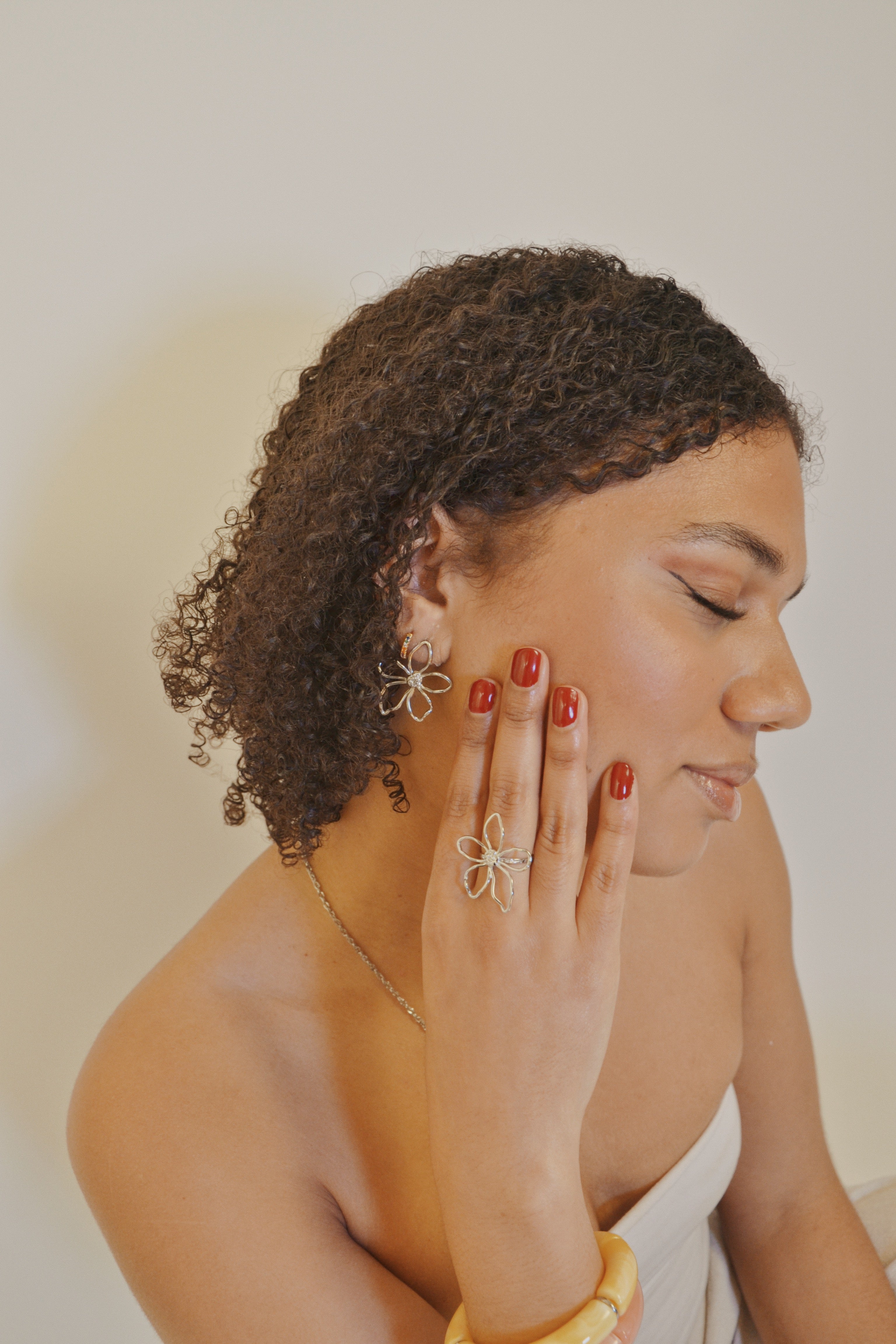 Femme portant bijoux fleur en or, bague et boucles d'oreilles, fond neutre, look élégant